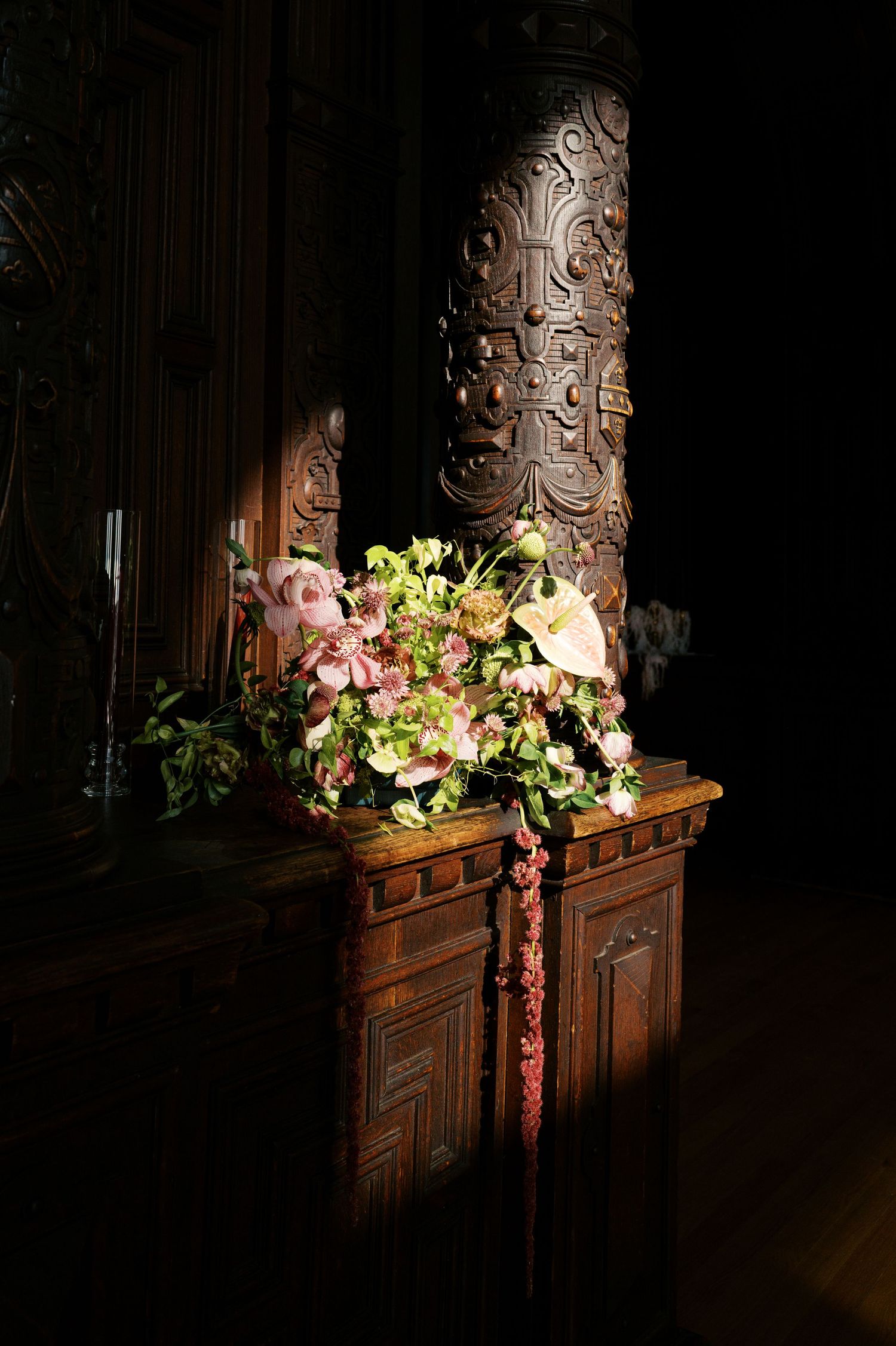 Ornate wooden church pew with floral arrangements of pink and yellow flowers against a dark carved backdrop.