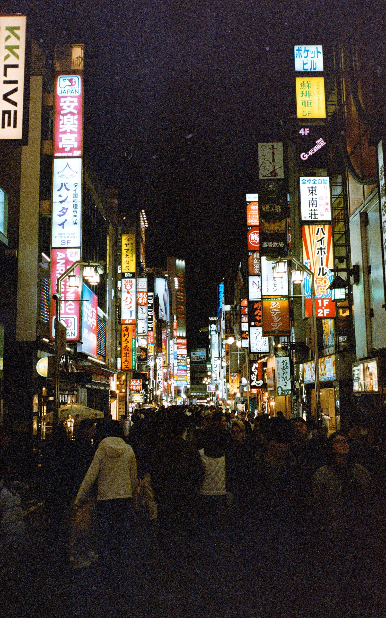 Bustling nighttime street in Japan with bright neon signs and advertisements illuminating the urban scene.
