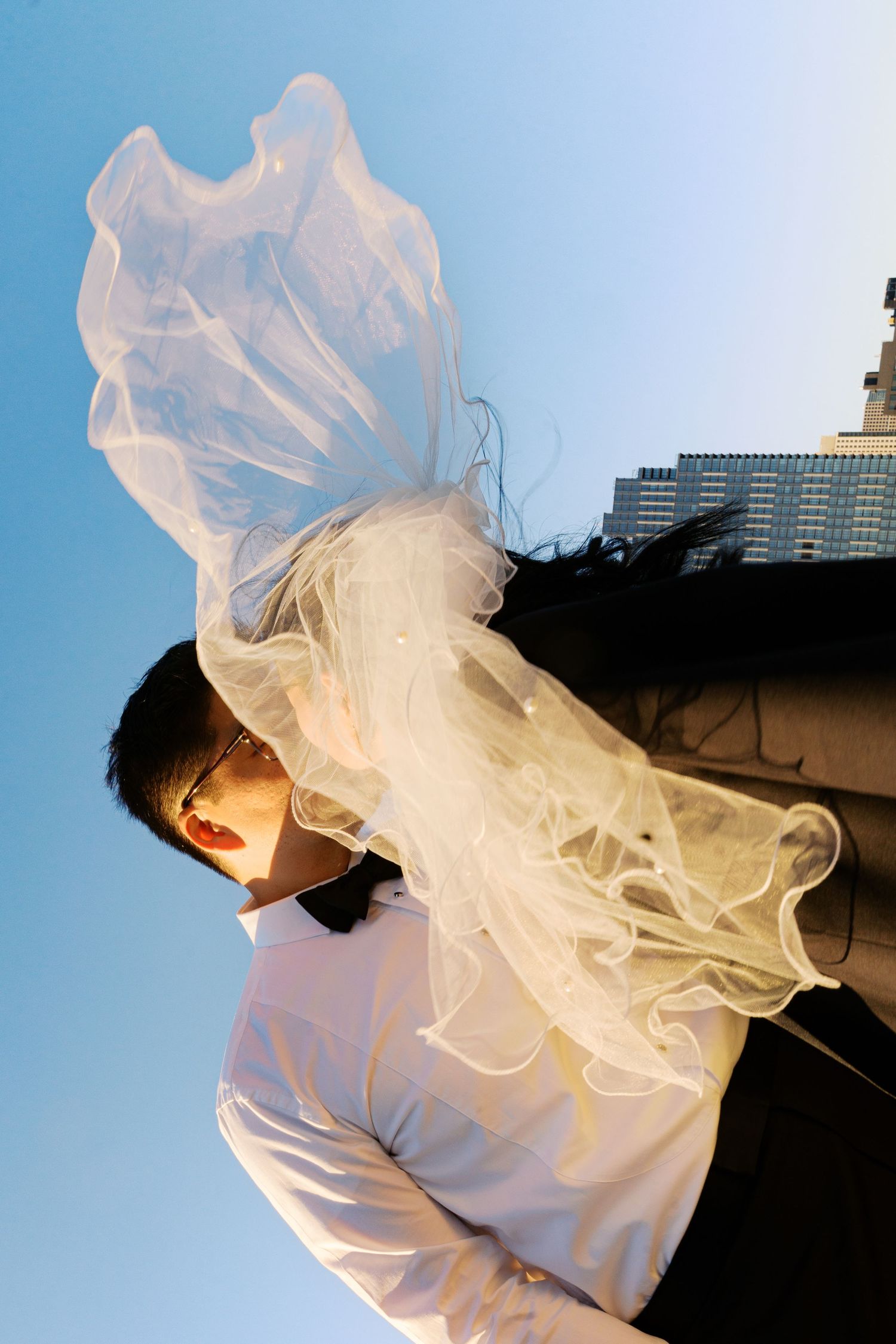 Flowing white veil catches breeze against blue sky in artistic wedding portrait.