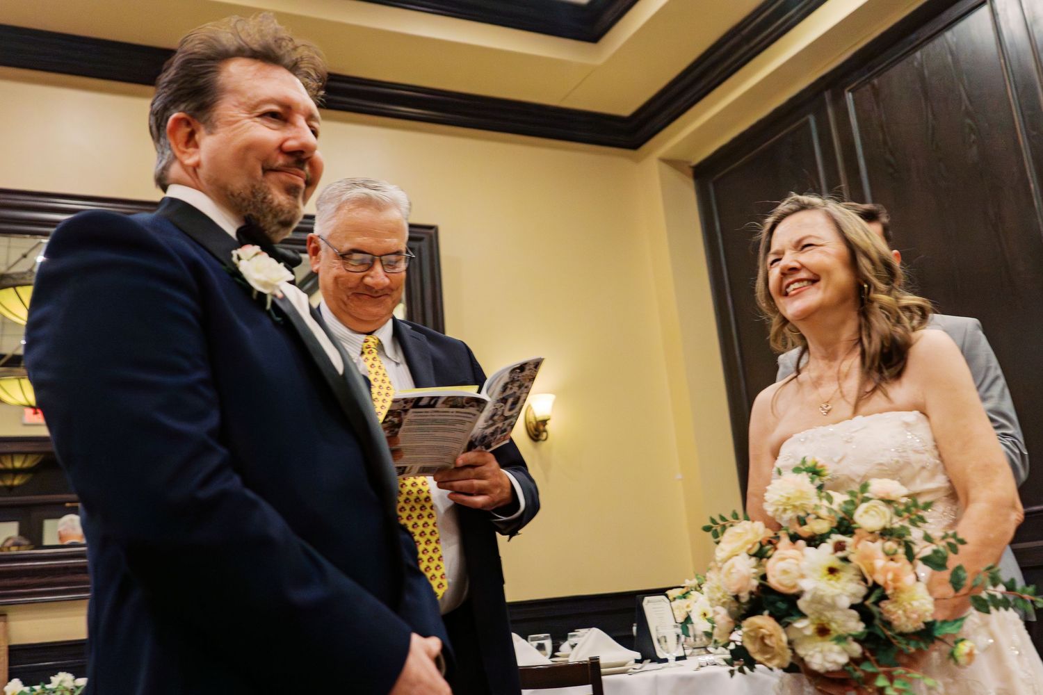 A joyful wedding ceremony moment with a couple and officiant sharing laughter during the vows.