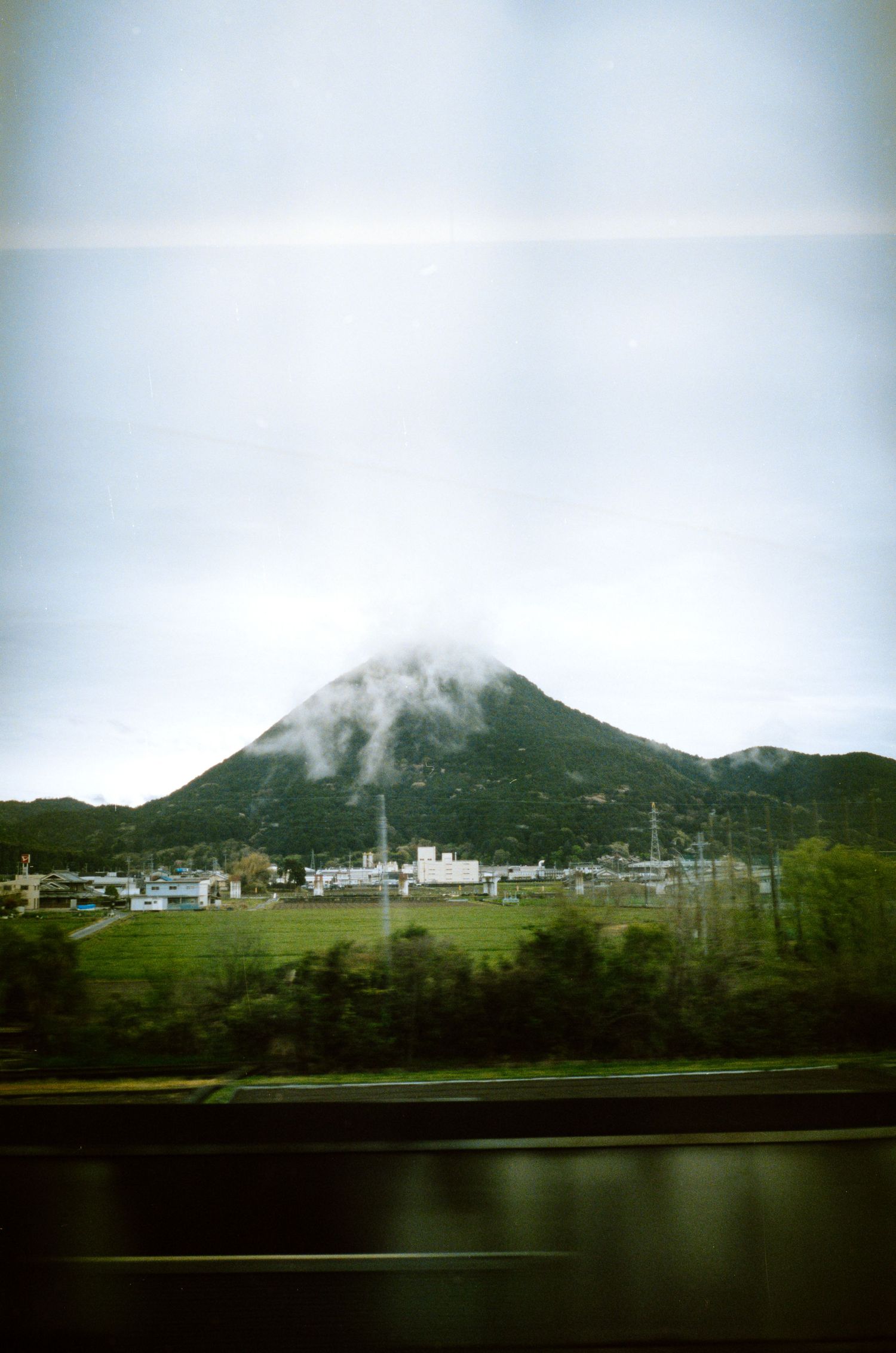 Misty mountain landscape with residential buildings nestled at its base near water.