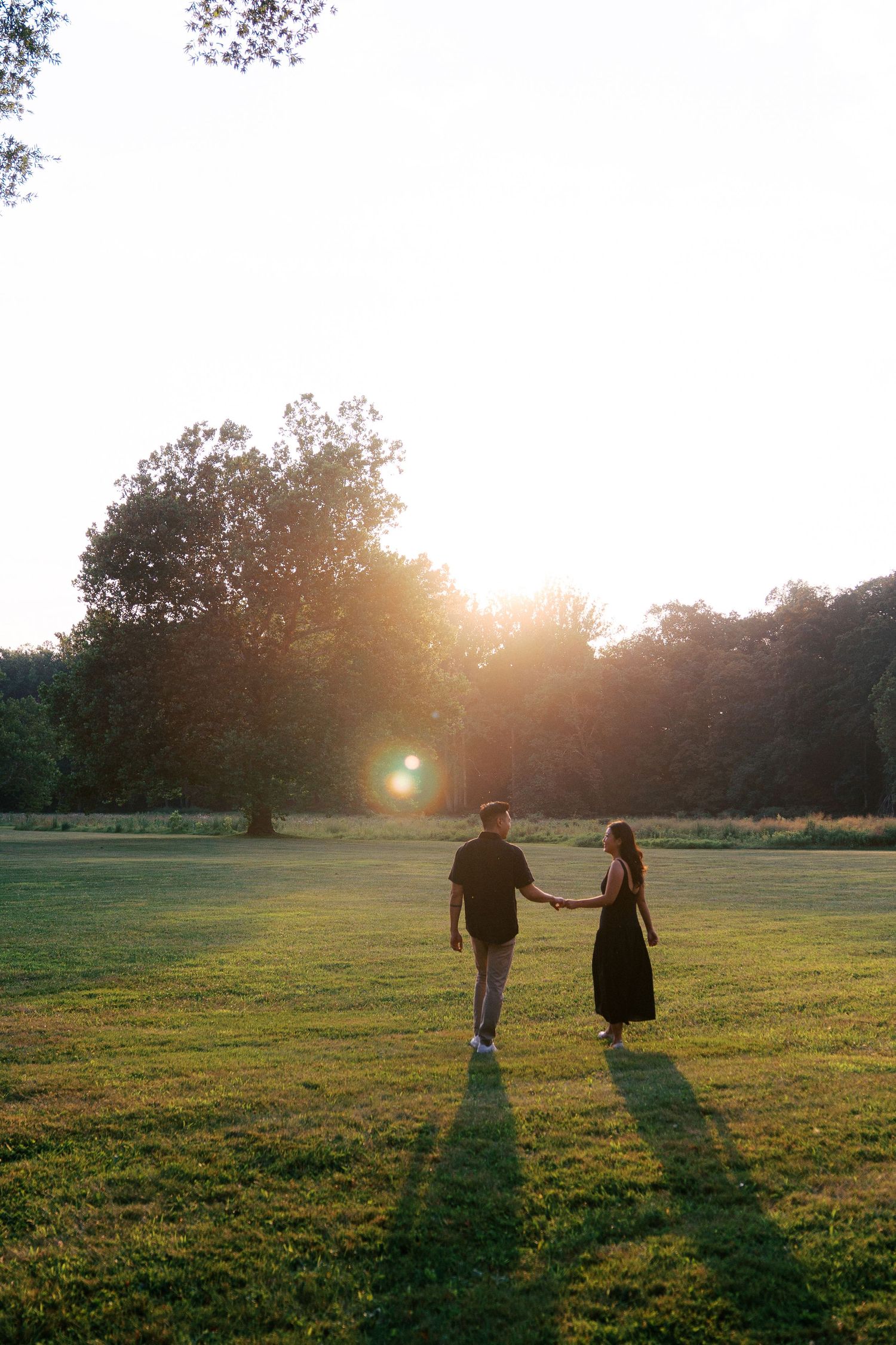 Two silhouettes walk across a sunlit grassy field during golden hour casting long shadows.