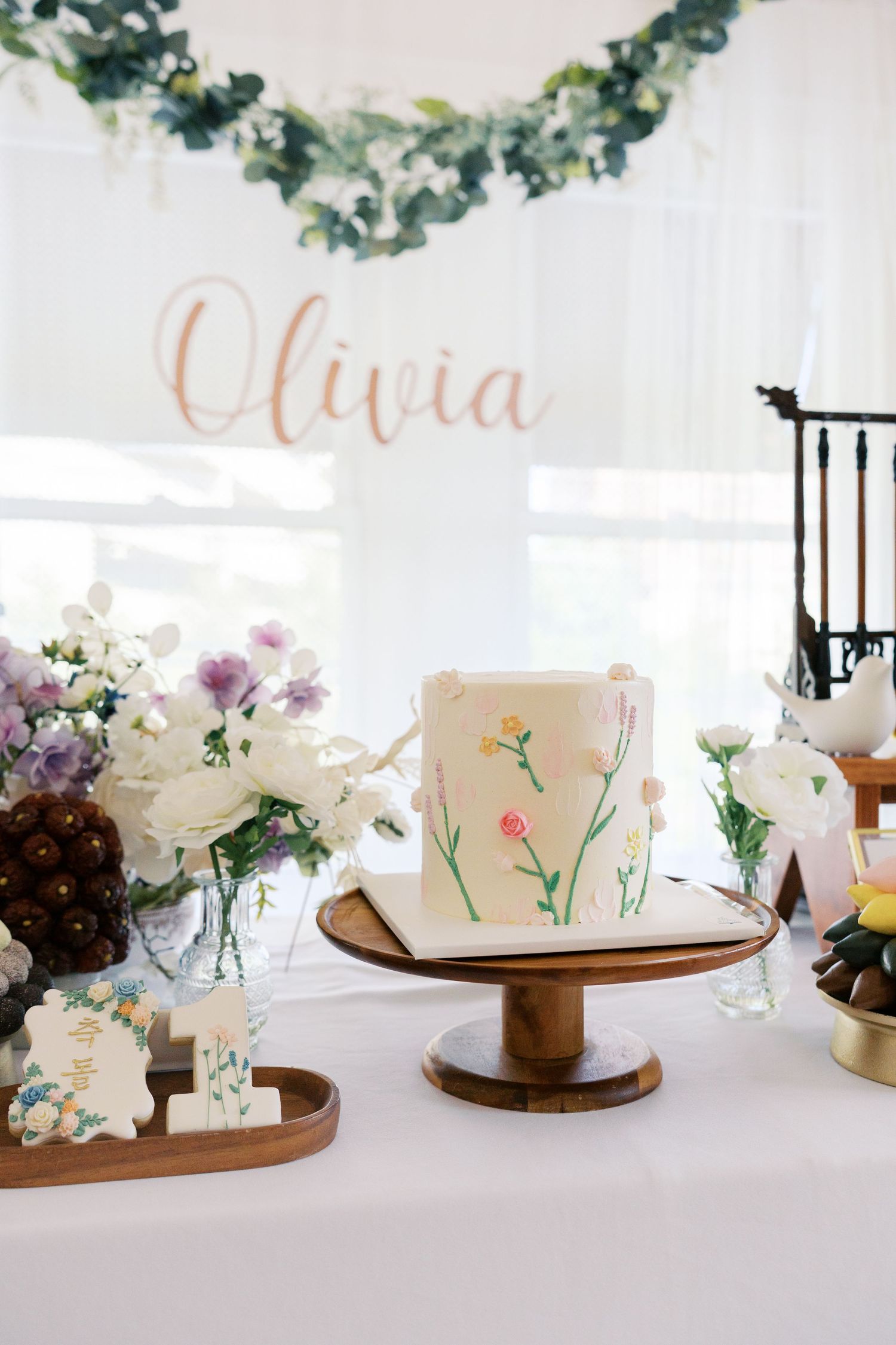 Elegant floral cake display with name 'Olivia' and greenery garland decoration.