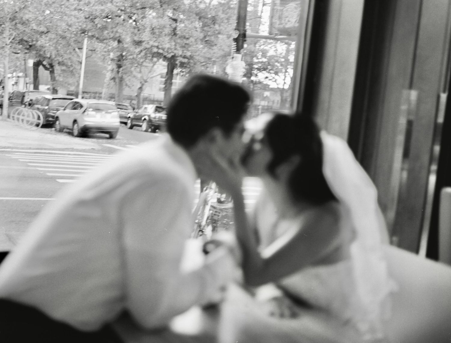 Four sequential black and white images show a couple in a romantic embrace sharing a kiss on a city street.