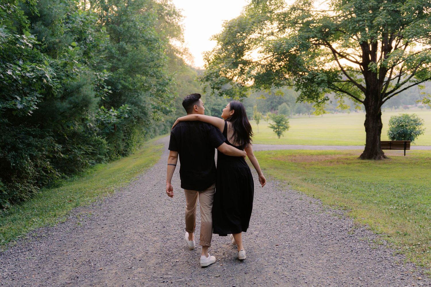 Two people walking together on a tree-lined path at sunset.