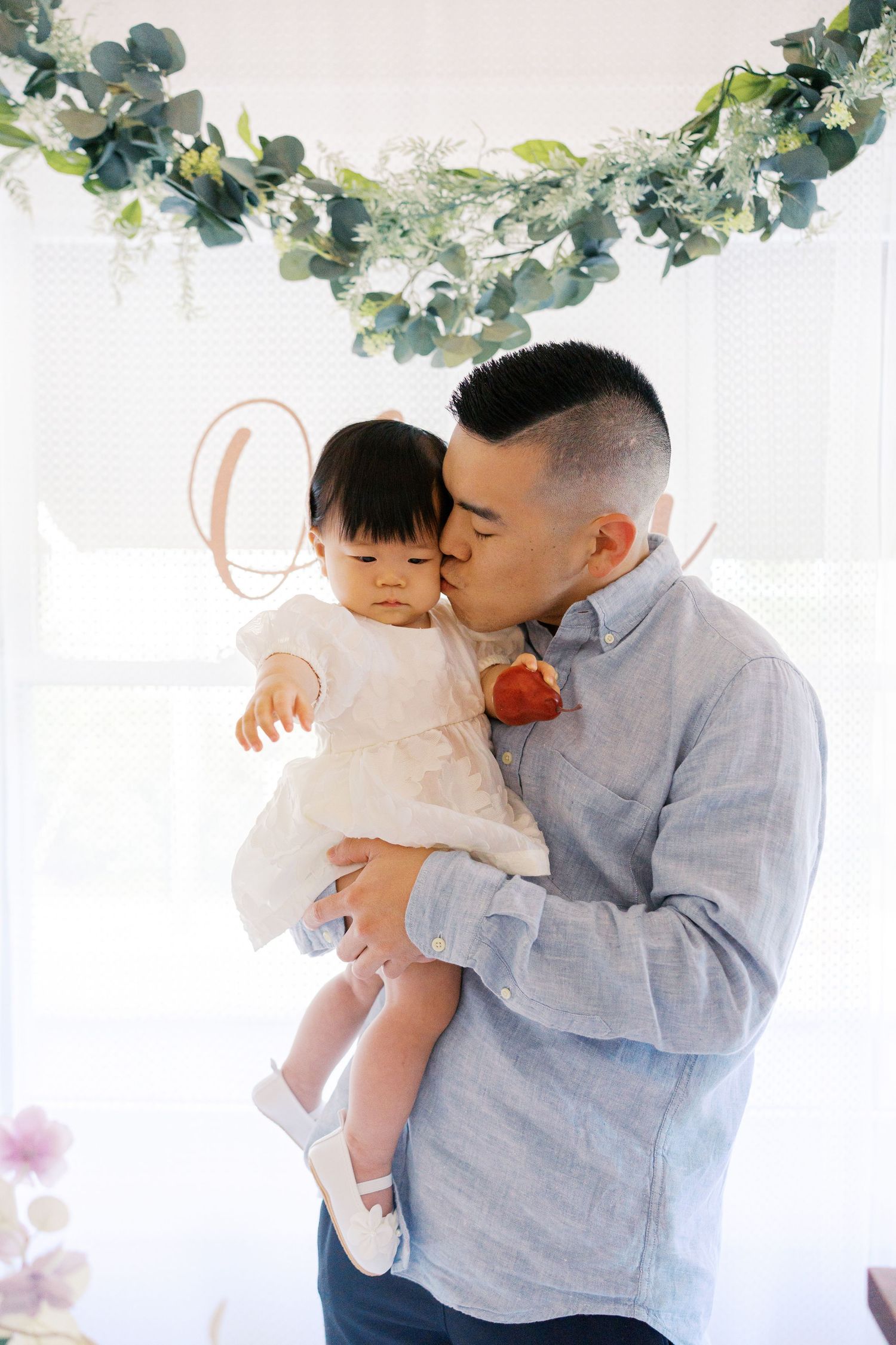 Sweet family moment captured against white backdrop with greenery garland decorations.