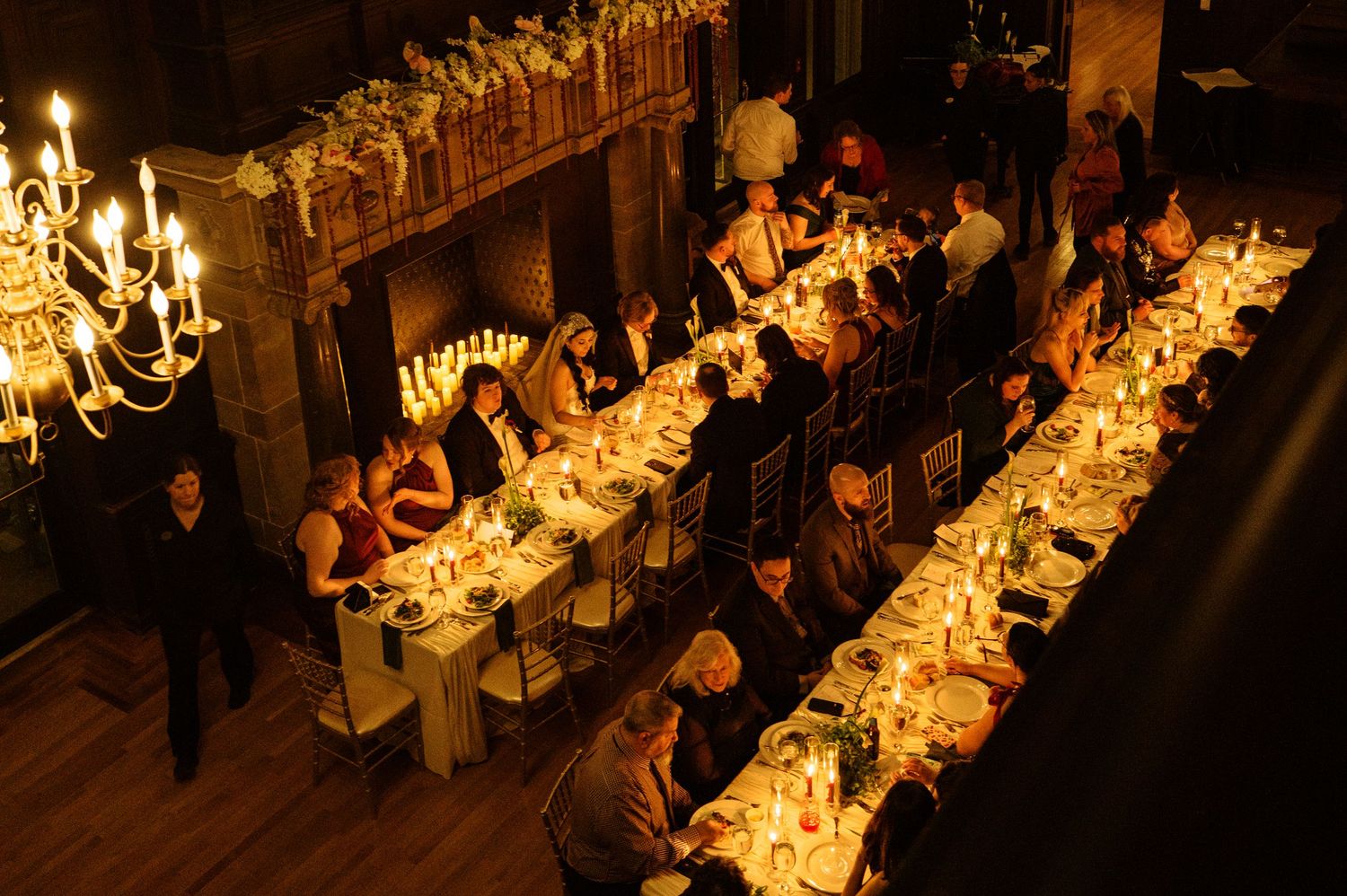 Elegant candlelit banquet tables extend down a long hall with ornate chandeliers and golden decor.