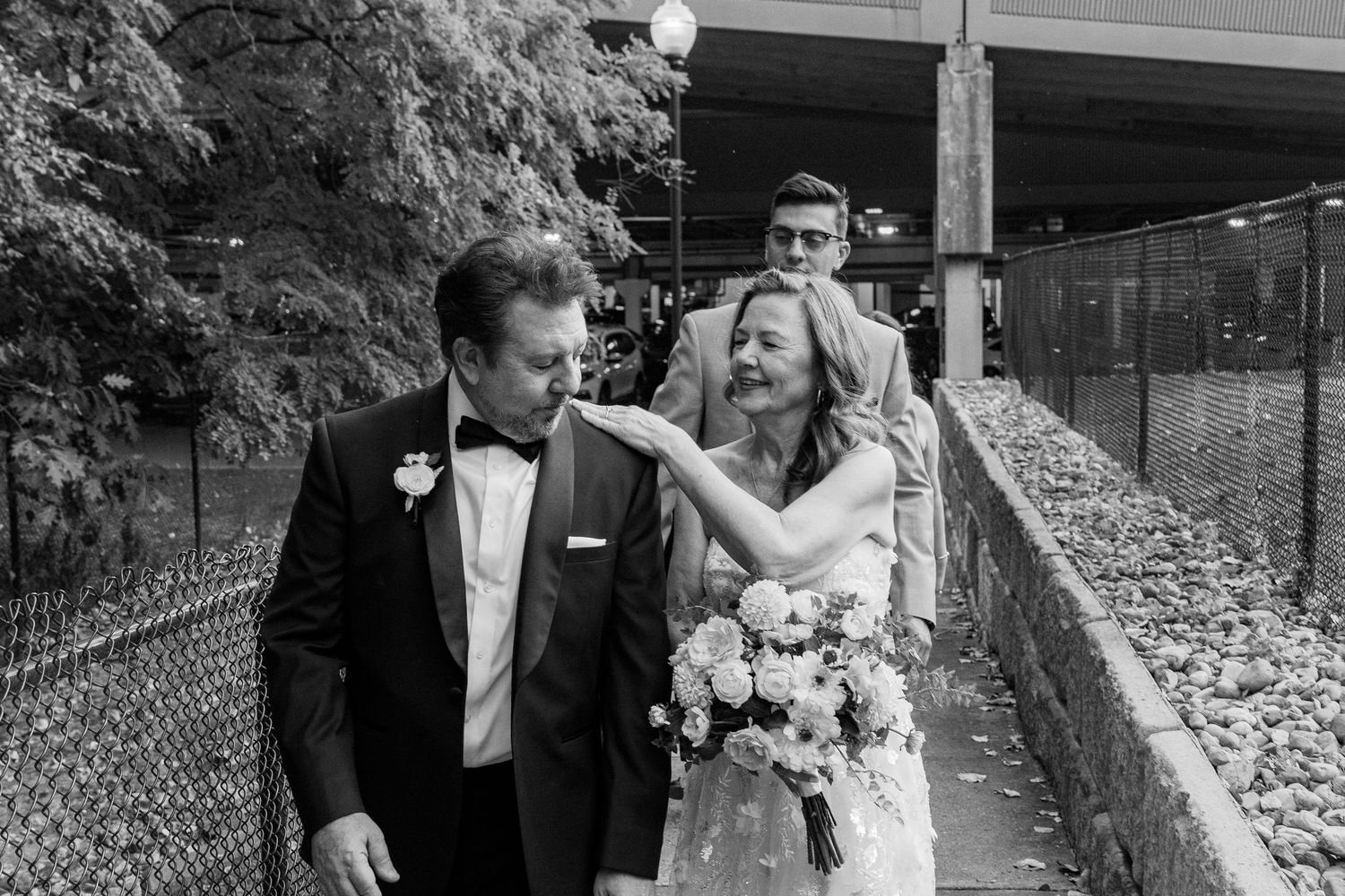 Black and white photo of a wedding couple sharing a playful moment on a path.