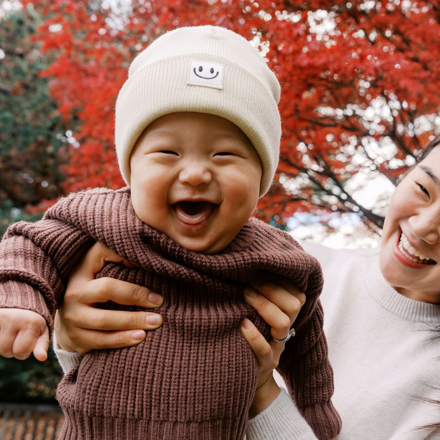 Candid expressions captured against vibrant red autumn foliage background.