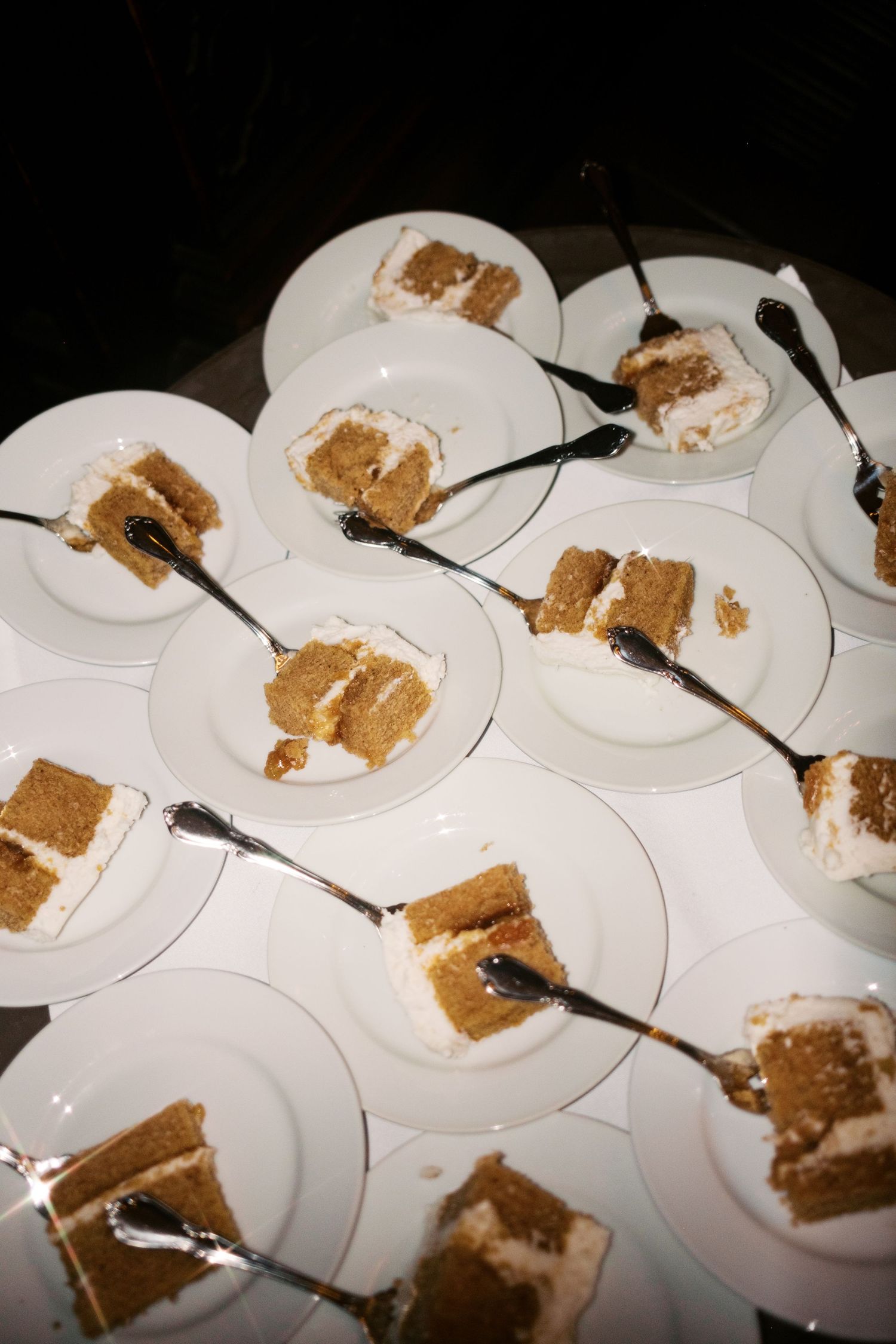 Multiple white plates with partially eaten slices of brown cake arranged in a diagonal line.