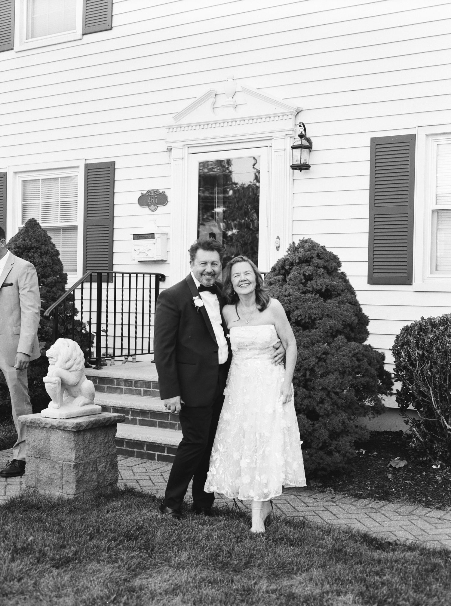 A couple laughs together on the front steps of a white colonial-style house.
