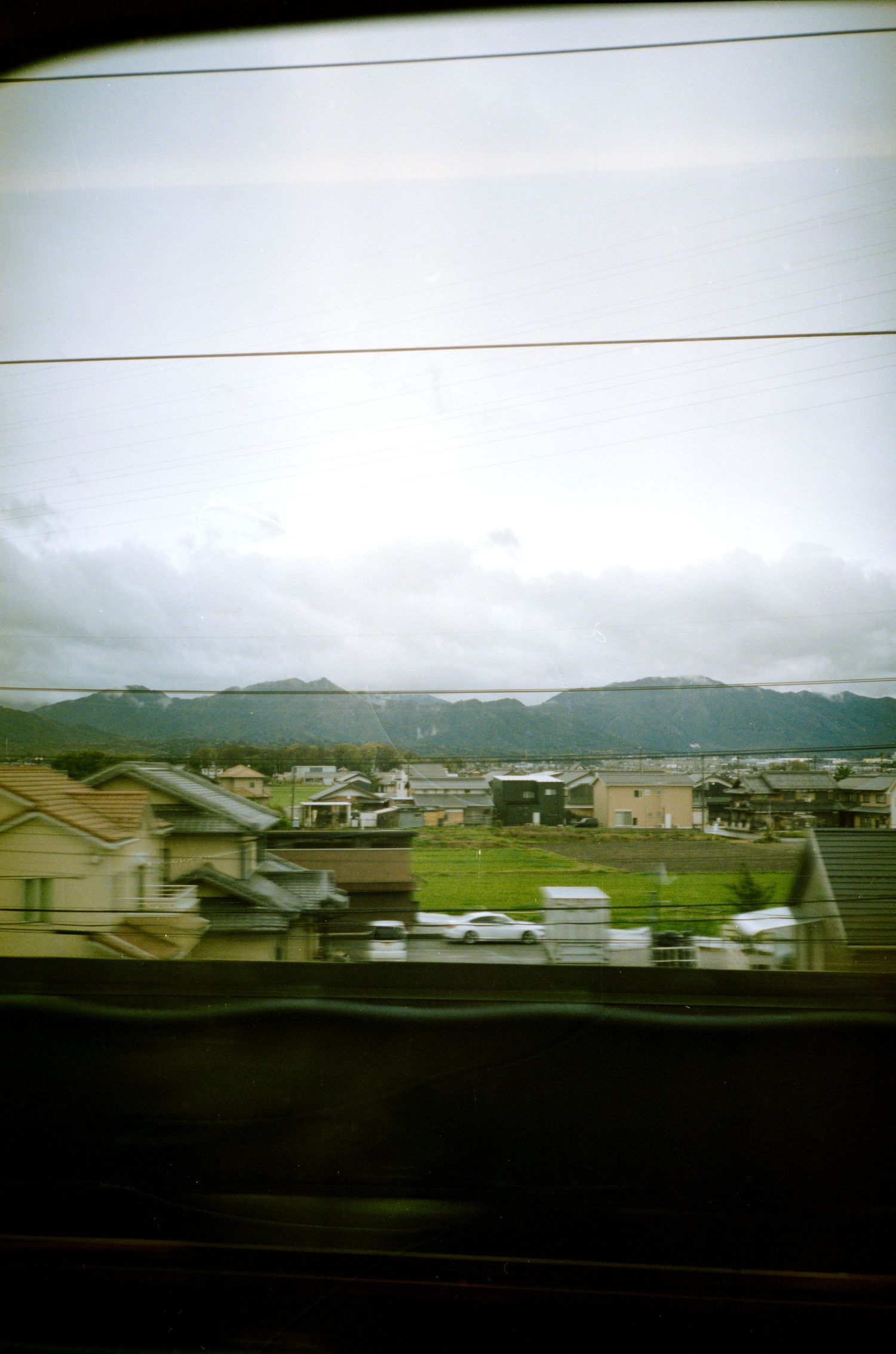 Suburban houses and buildings seen from moving vehicle with mountains in background.