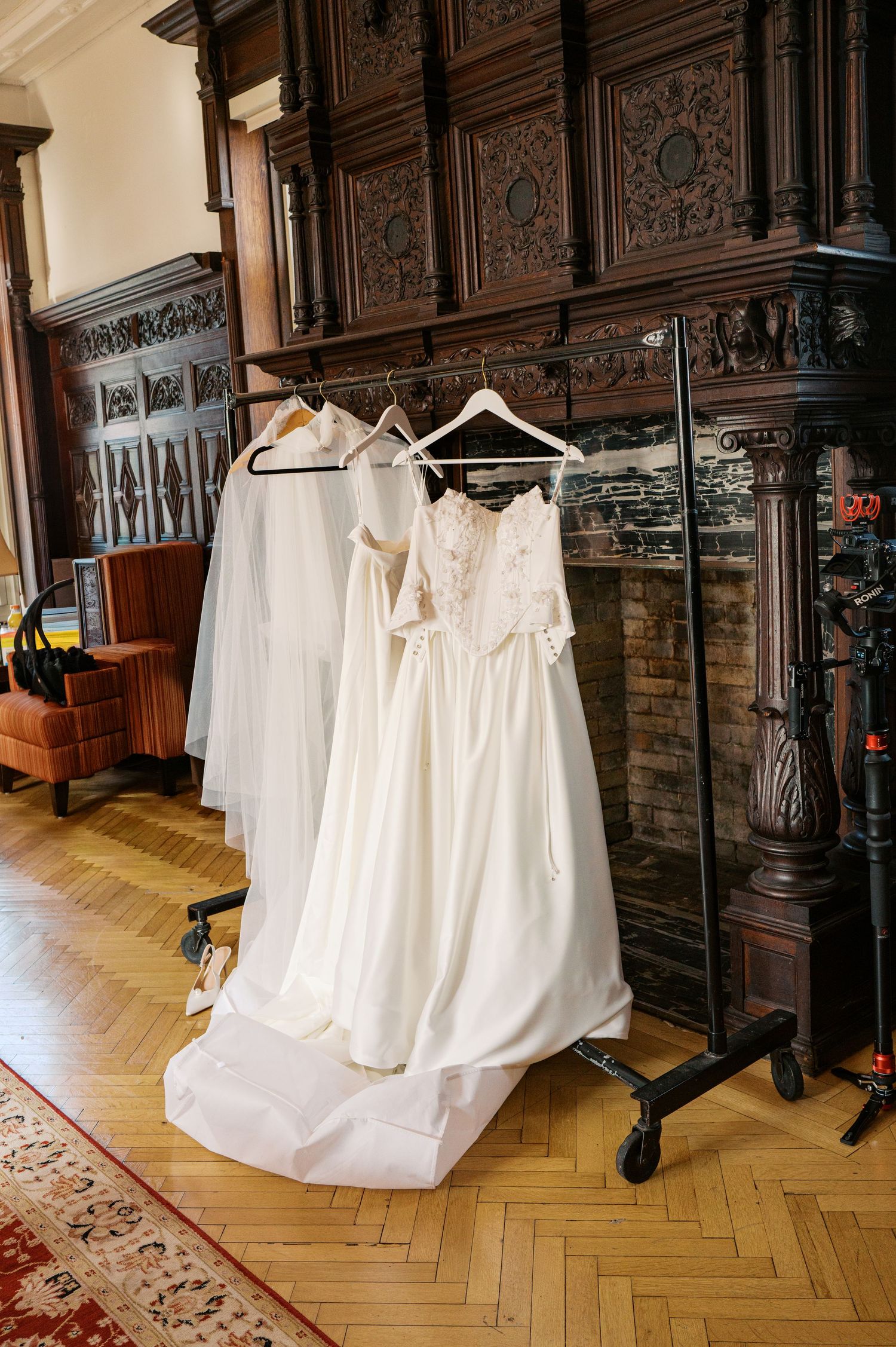 A collection of white wedding dresses displayed on hangers in an elegant room with ornate wooden paneling and herringbone floors.