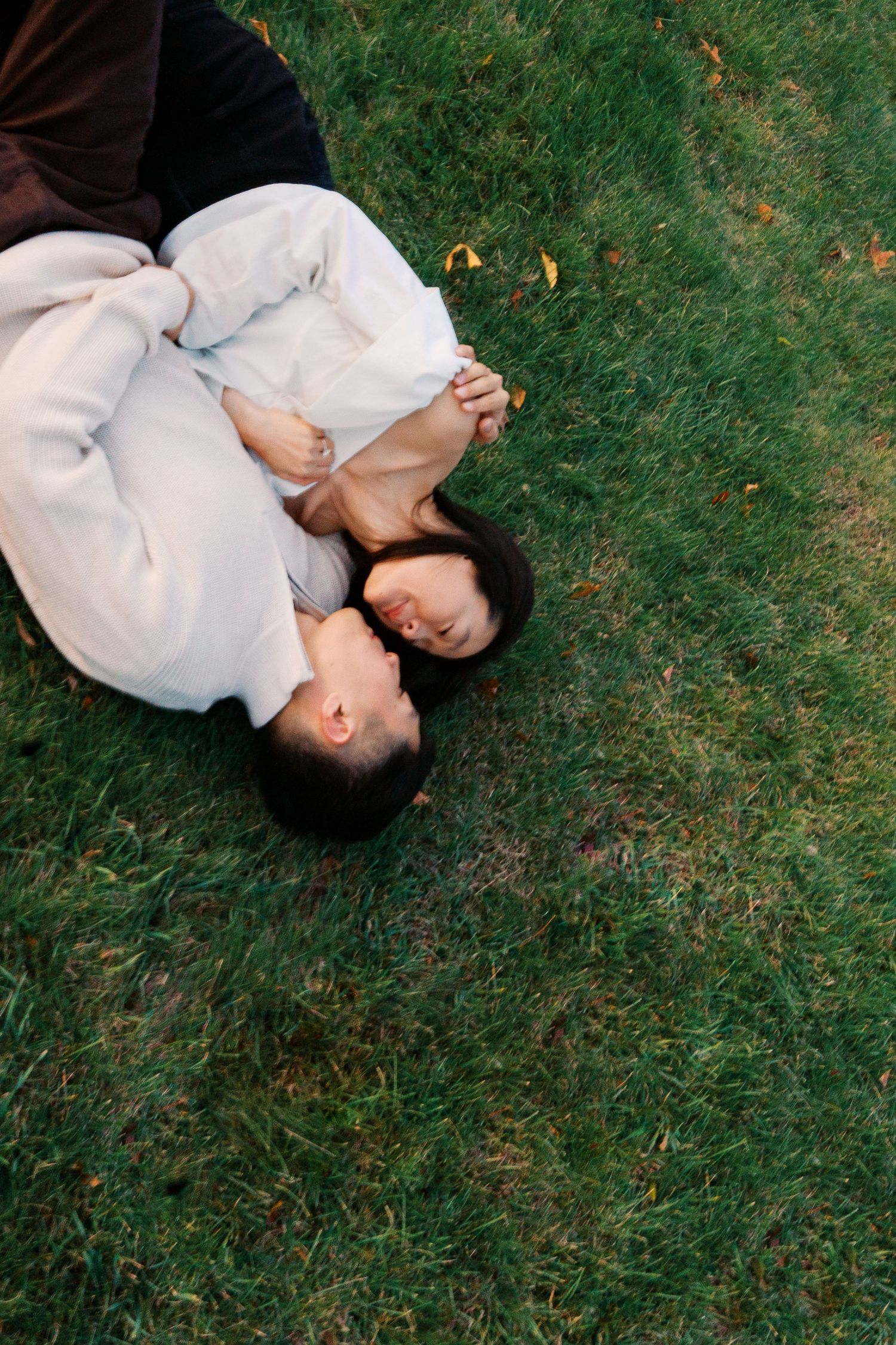 Two people in white clothing lying on green grass in a peaceful moment.
