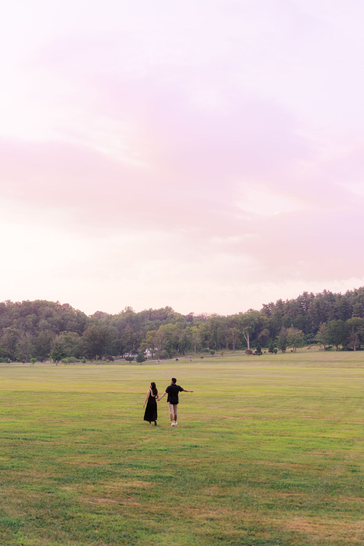 Distant figures walking across an expansive grassy field during sunset.