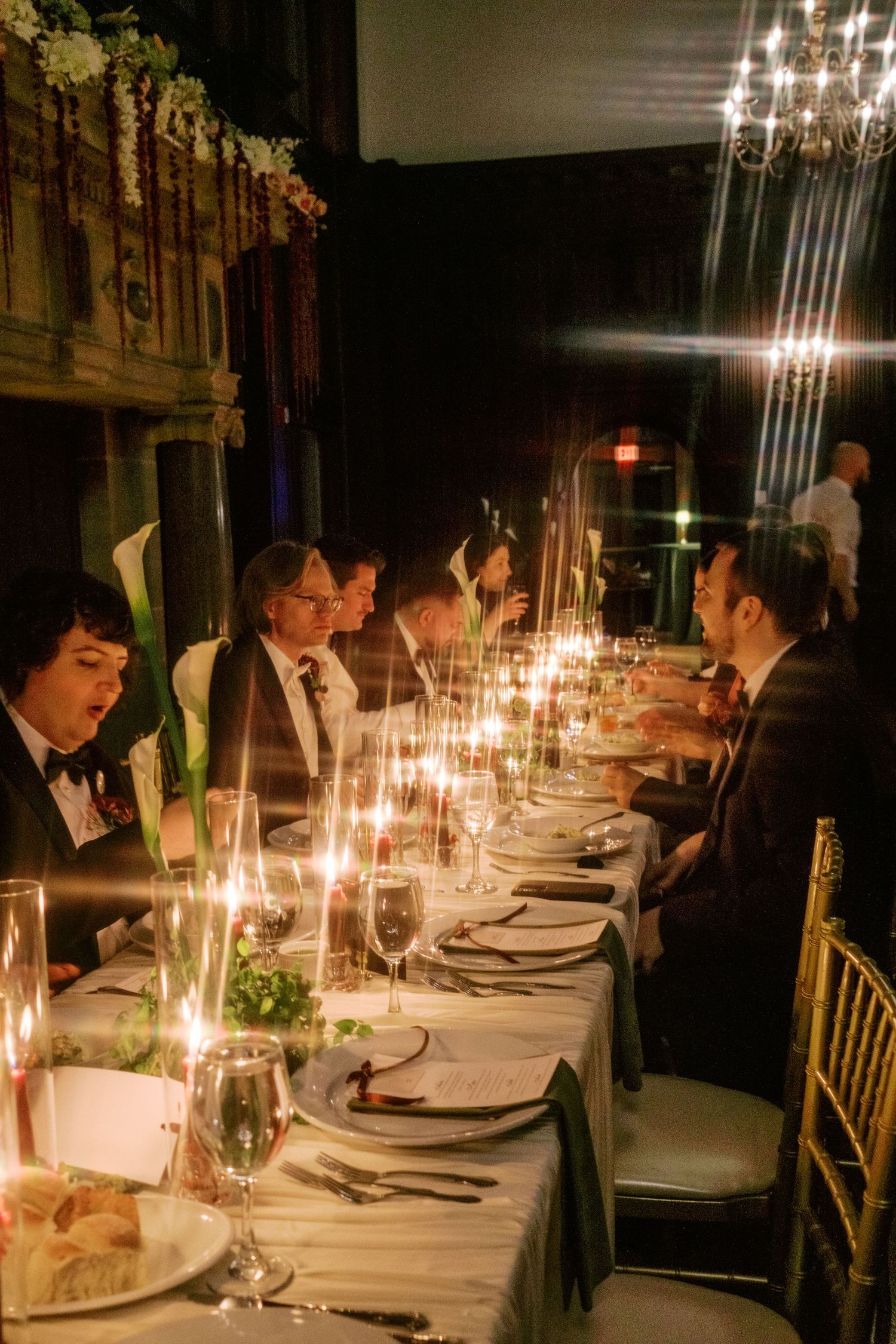 Elegant candlelit dinner table set with formal place settings and crystal chandeliers in a dimly lit dining room.