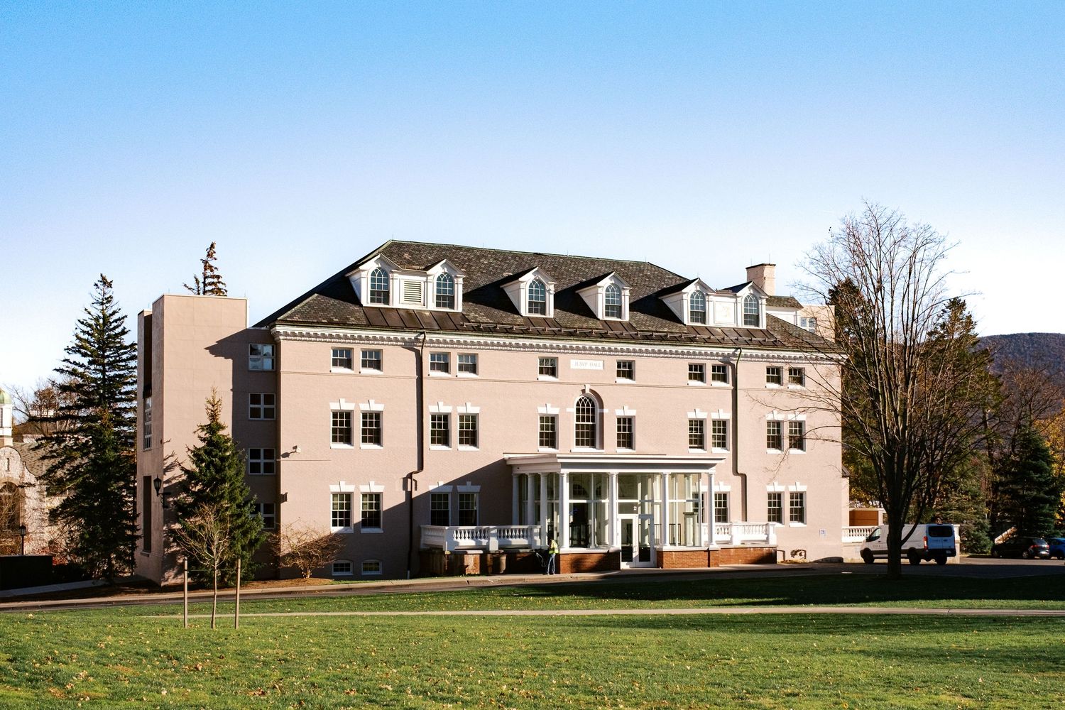 Colonial-style three-story building with dormers and white trim set against a clear blue sky.