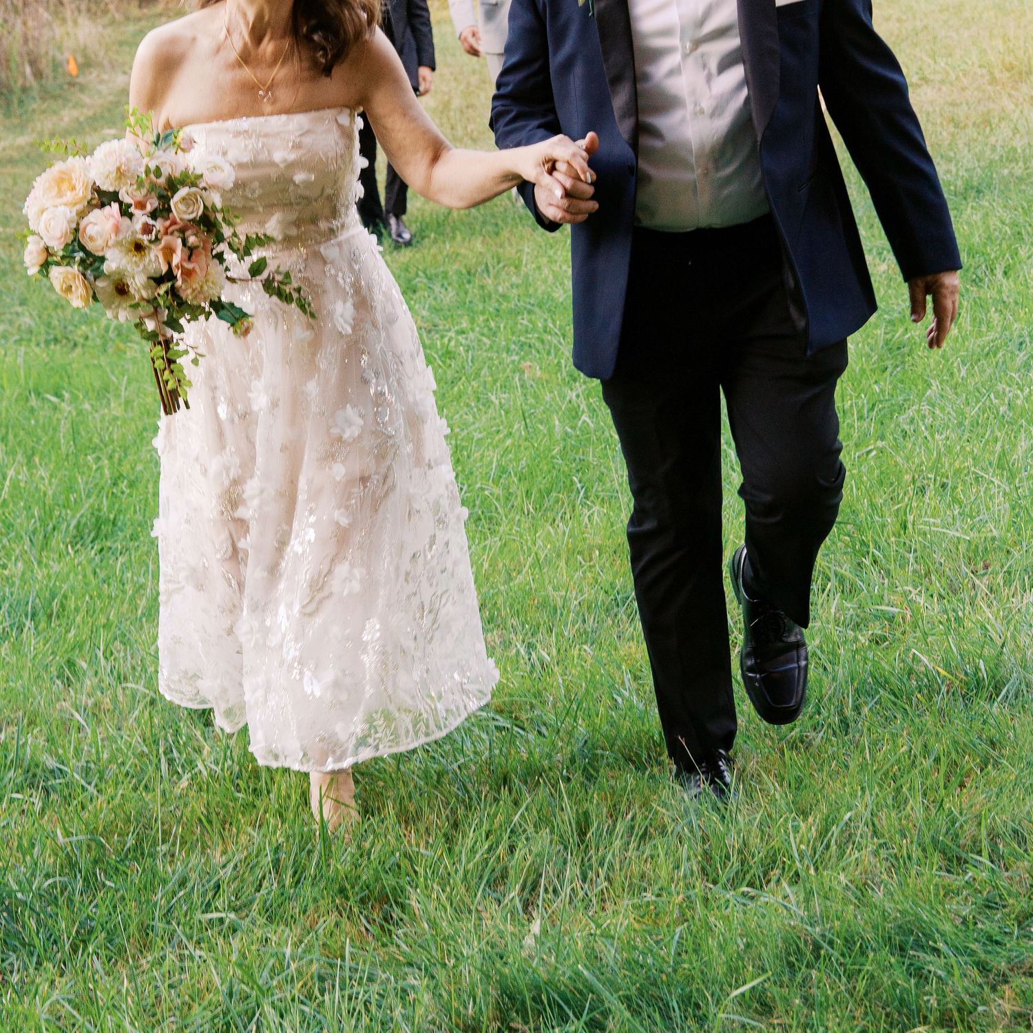 Wedding party walking together on grass in formal attire.