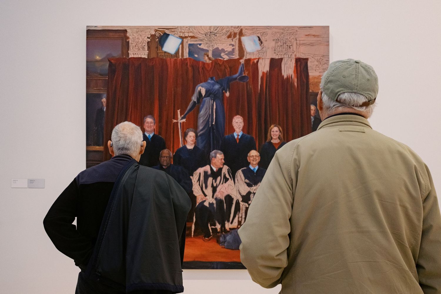 Gallery visitors in casual attire view artwork displayed on wooden walls in a museum exhibition space.
