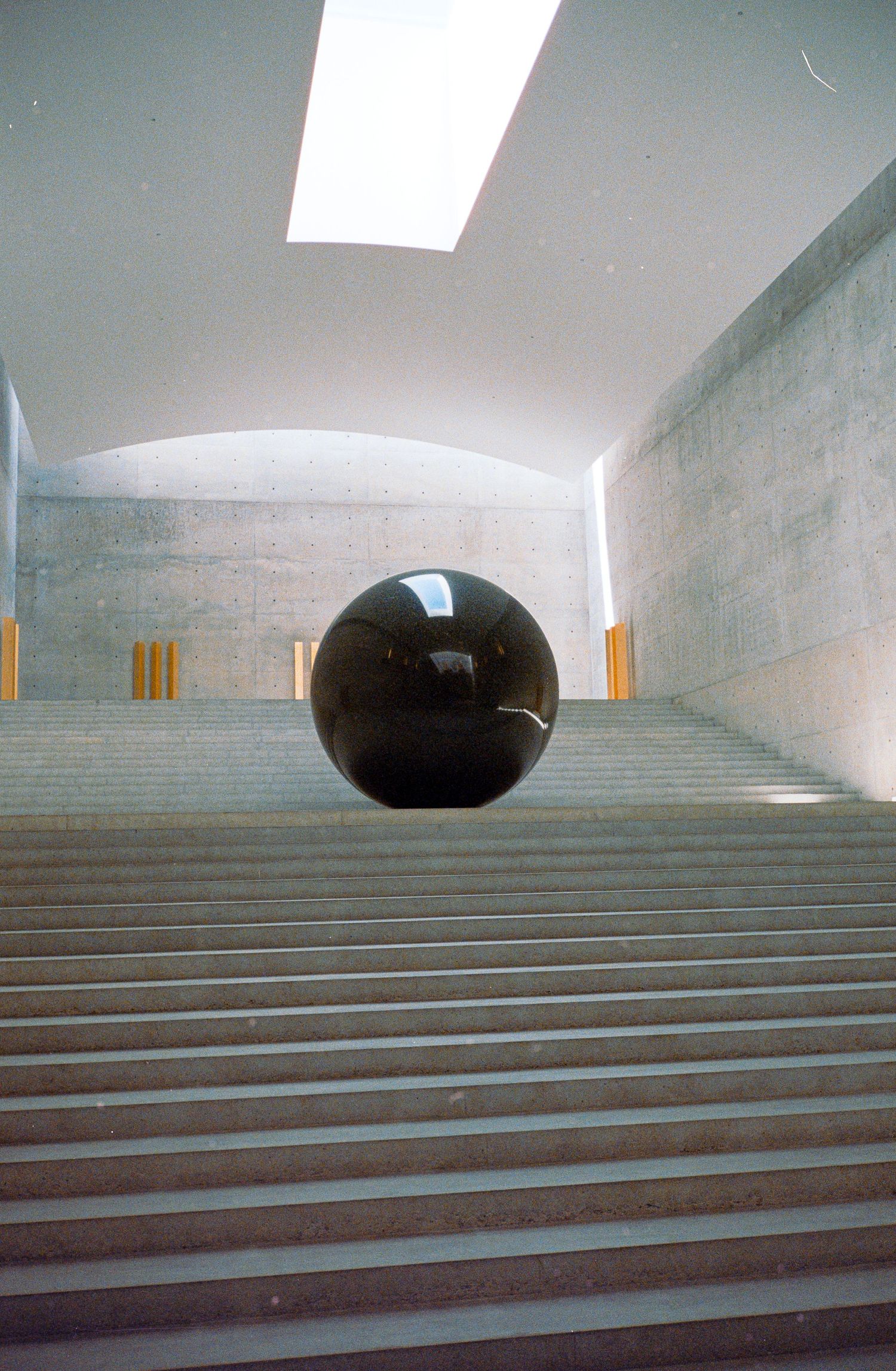 Sequence showing a large black sphere moving across concrete steps in an architectural space.