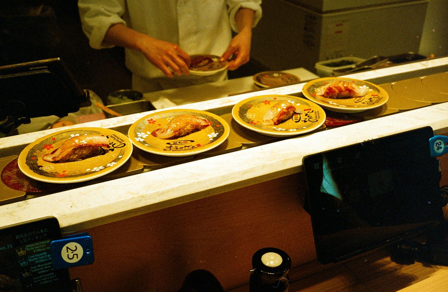 Row of plated meals being prepared on long white counter in restaurant kitchen.