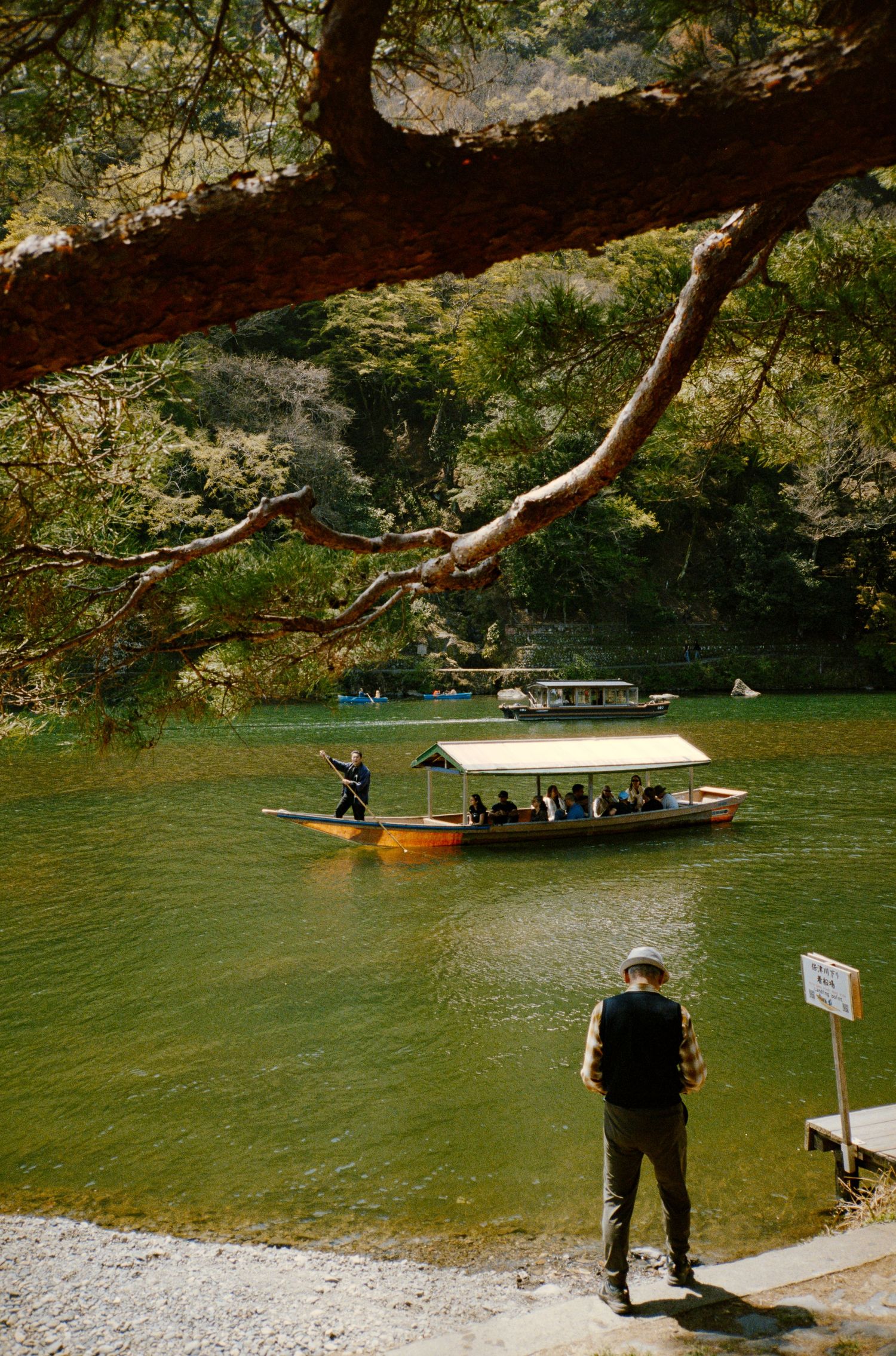Small boat docked at a tranquil river surrounded by overhanging trees and rocky cliffs.