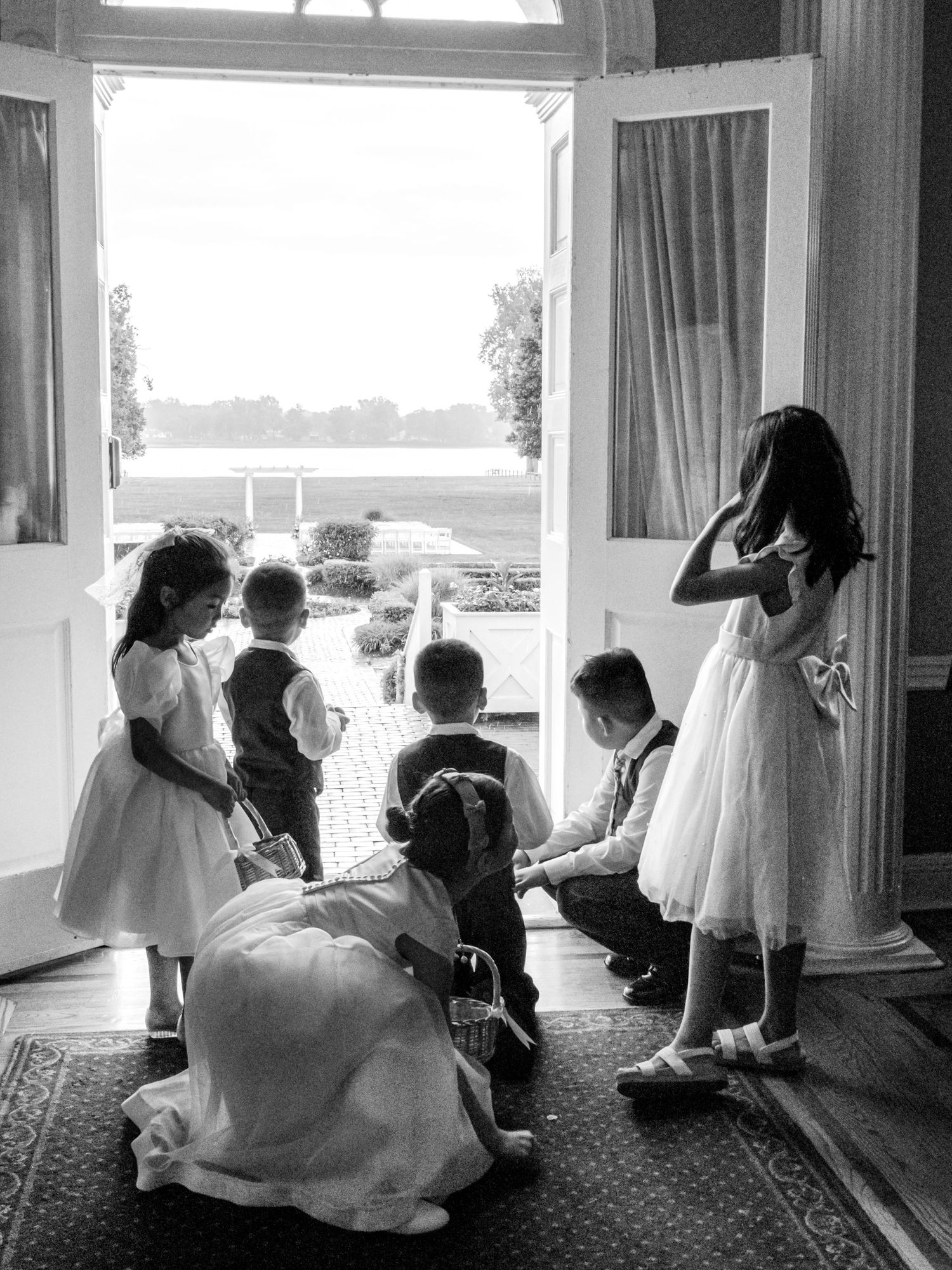 Black and white photo of flower girls and ring bearers gathered by open doors at a wedding venue.