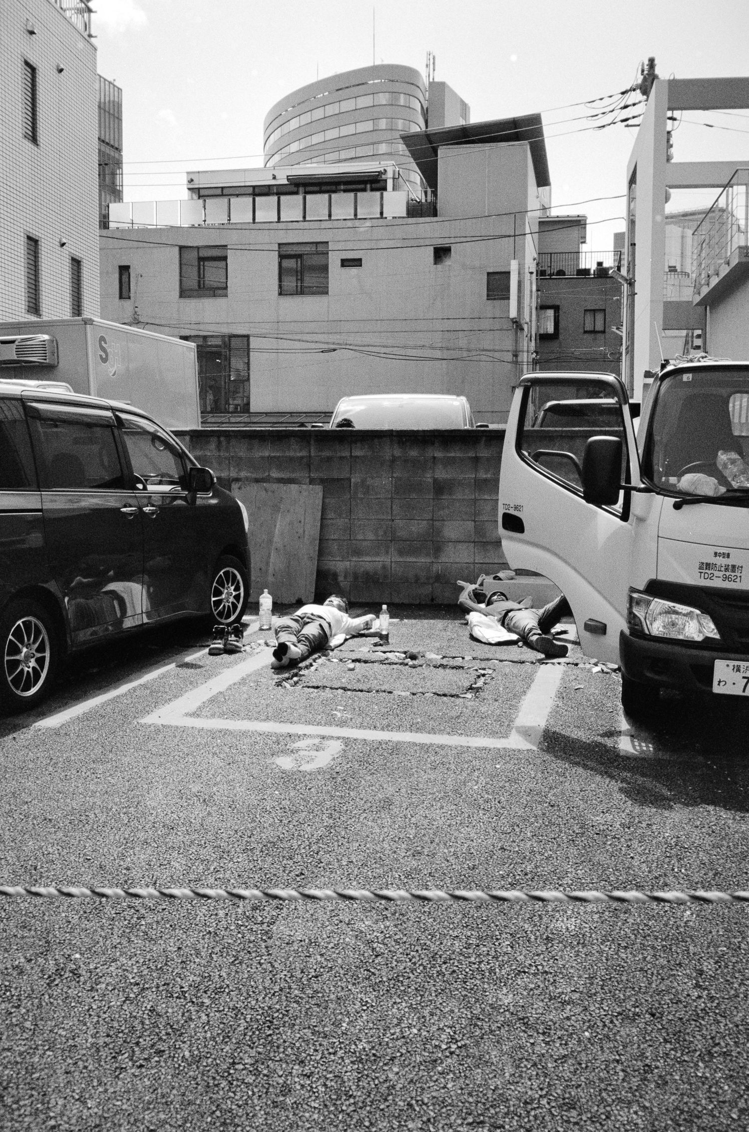 Black and white urban parking lot with vehicles and buildings in industrial setting.