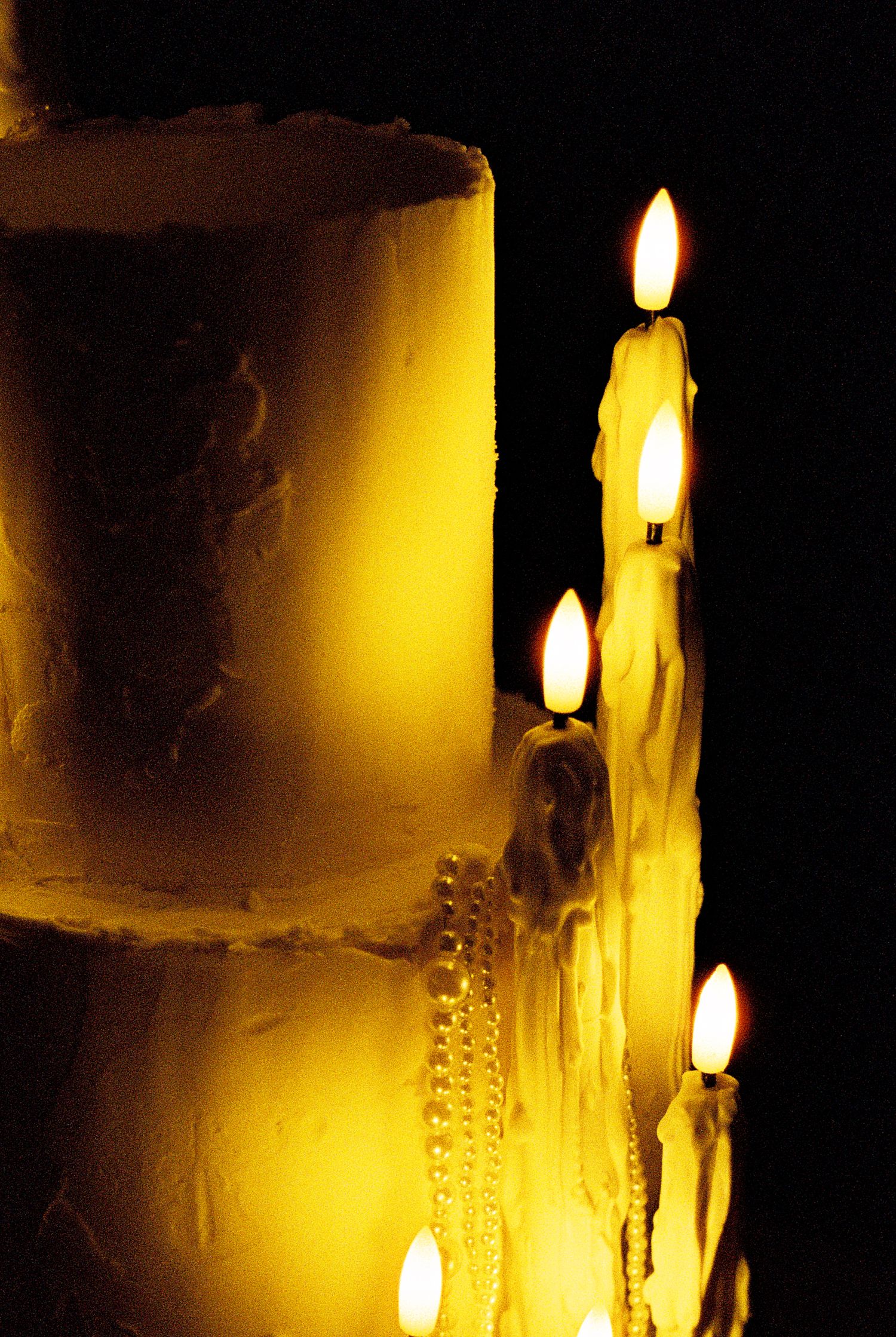 Several lit white candles glowing with warm yellow light against dark background create an atmospheric mood.