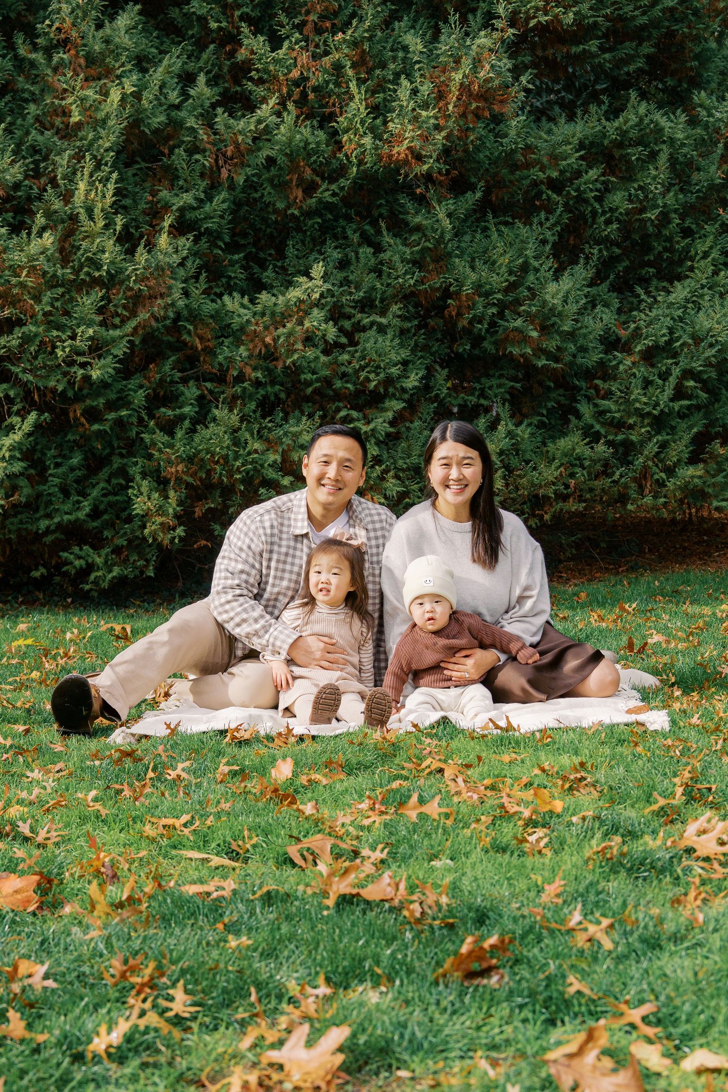 Family of four having a picnic on blanket surrounded by autumn leaves and evergreen trees.