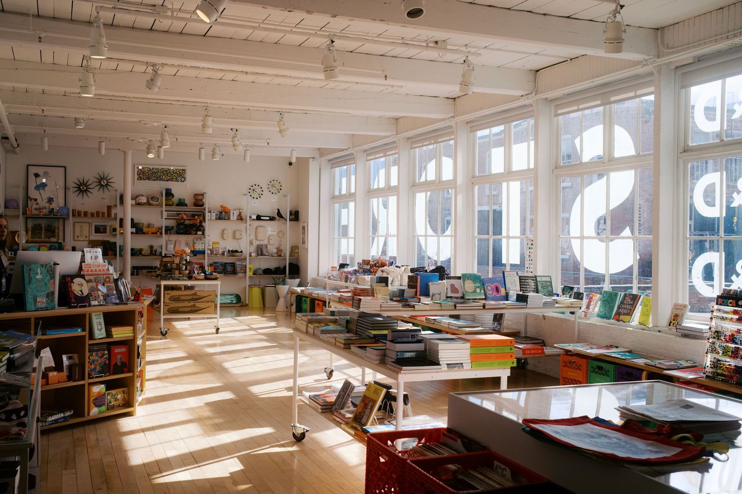 Sunlit open office space with bookshelves, modern furniture, and large windows creating a bright creative workspace.