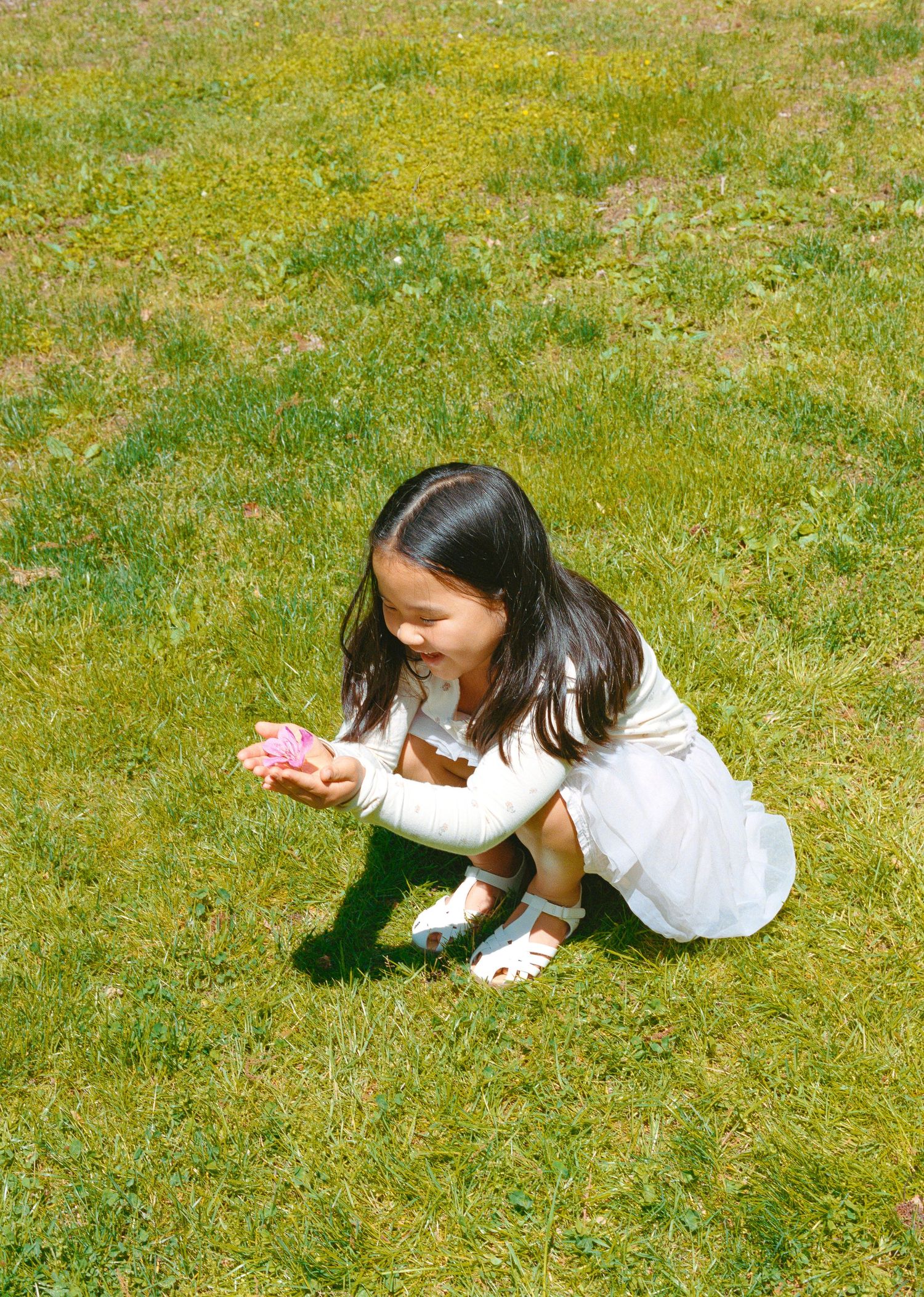 Child in white dress playing and crawling on grass in a garden setting.