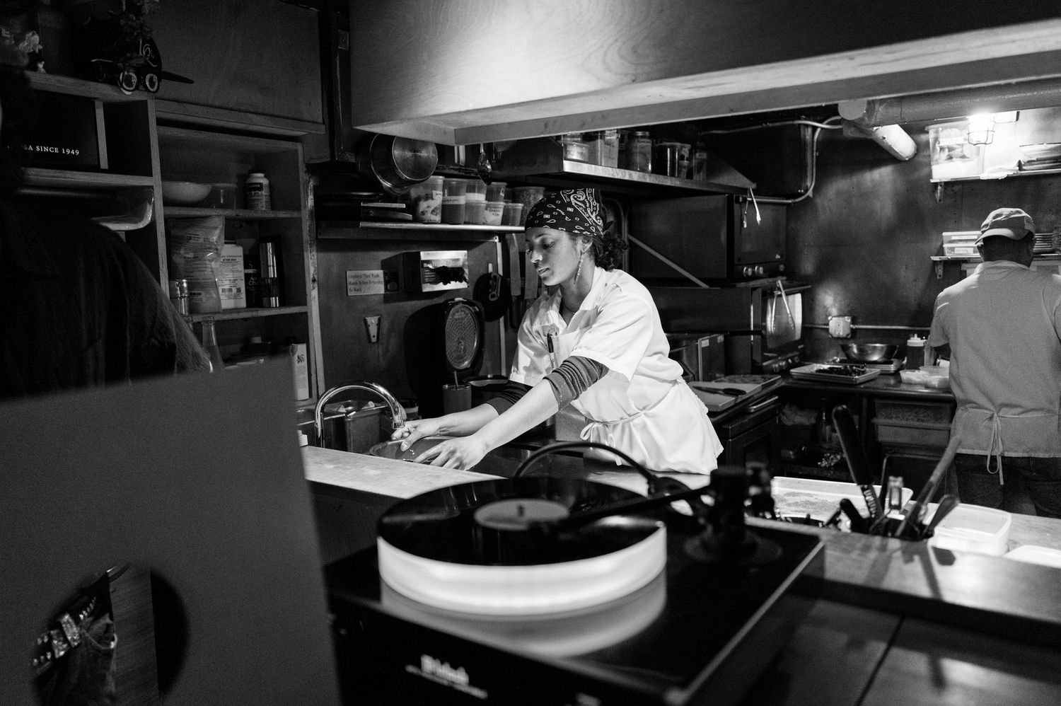 A black and white panoramic view of a restaurant kitchen with stainless steel equipment and work stations.