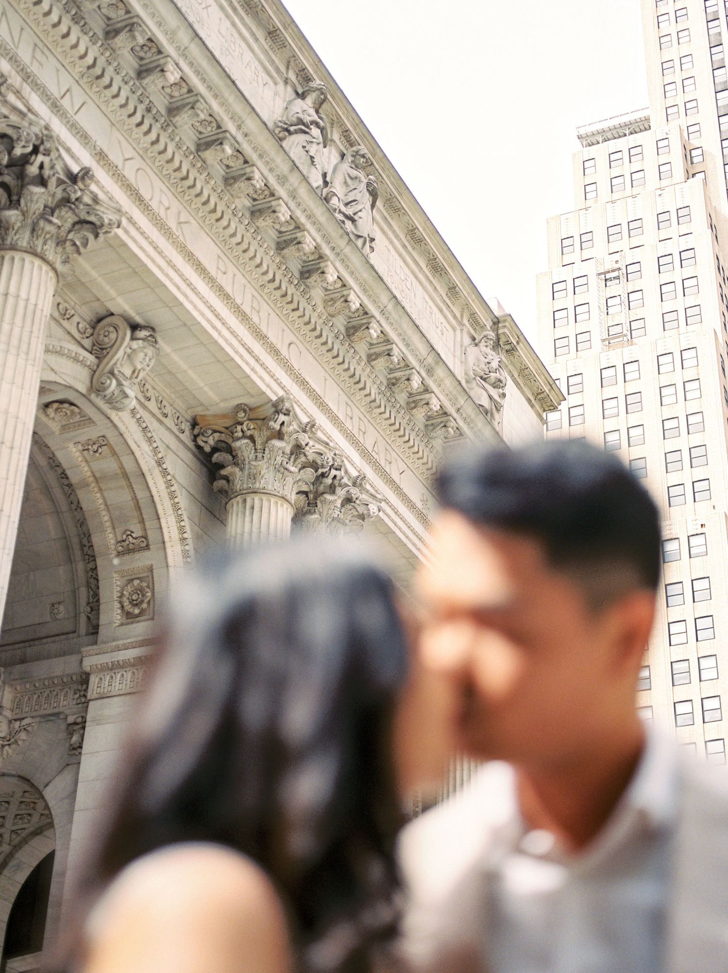 Couple sharing a kiss in front of a grand neoclassical building with ornate columns in New York City.