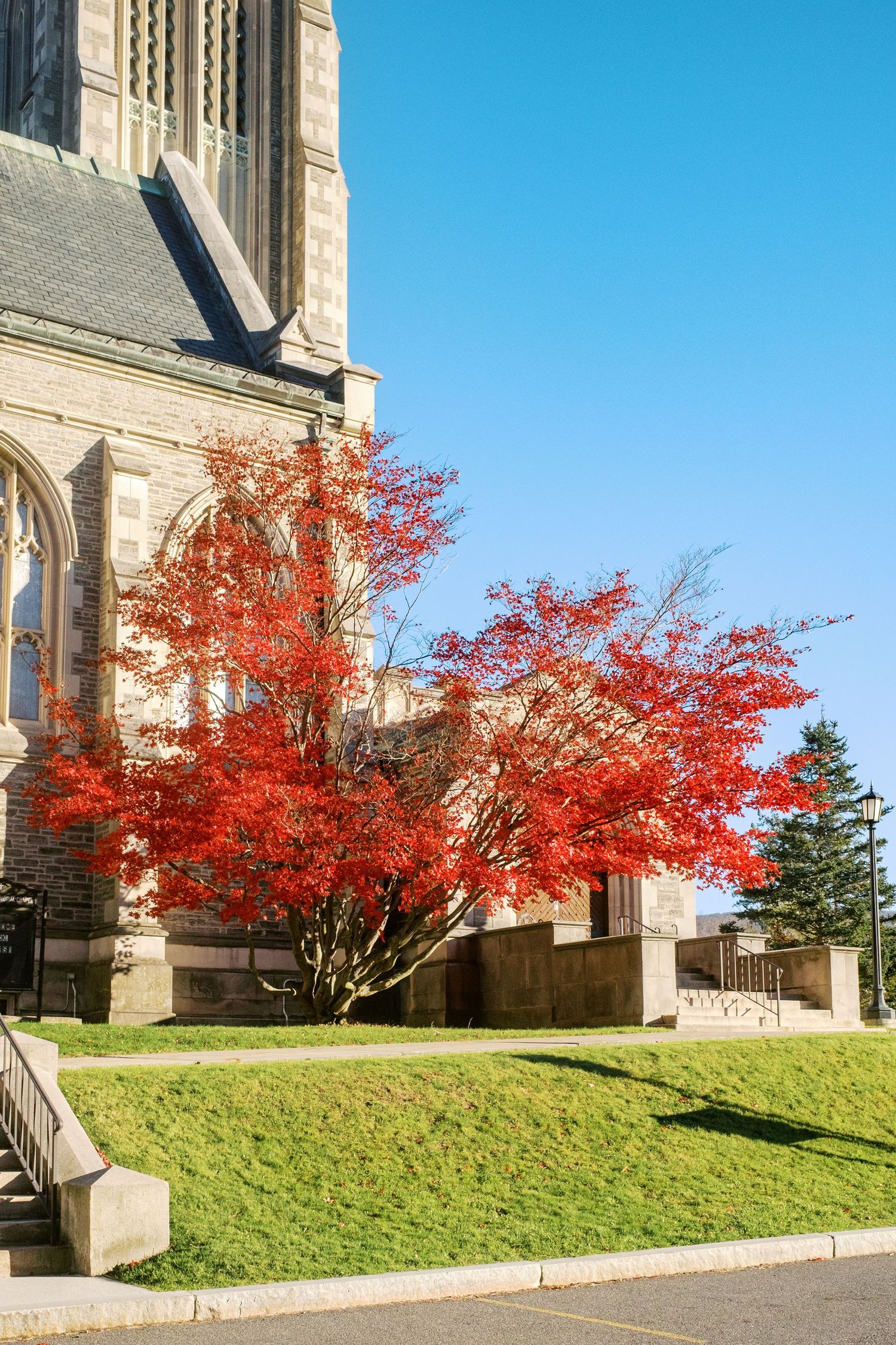 Vibrant red maple trees contrast beautifully against a stone church facade on a grassy hillside during autumn.