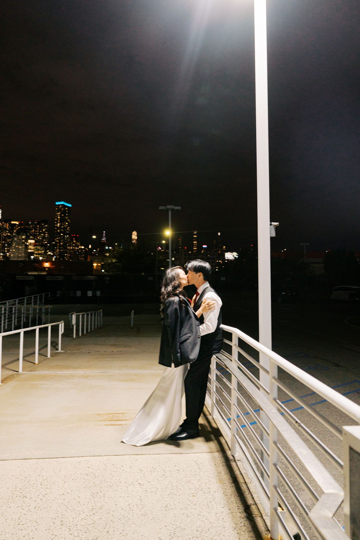 Wedding couple silhouetted against nighttime cityscape with illuminated buildings.