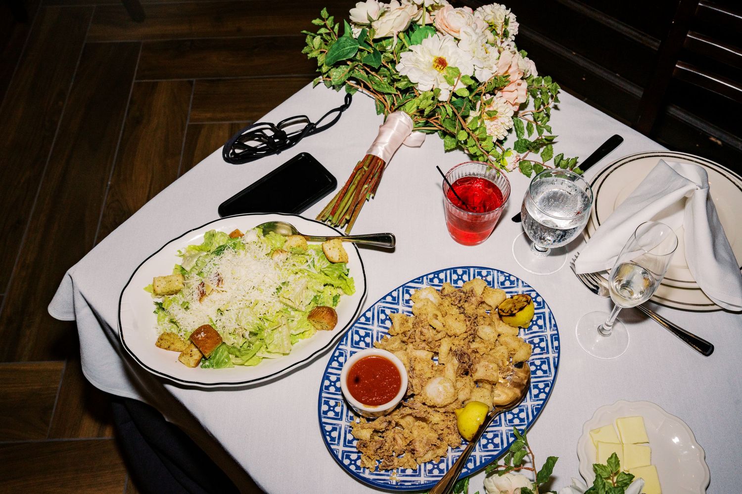 Wedding reception table set with salad, appetizers and floral decorations on white linens.