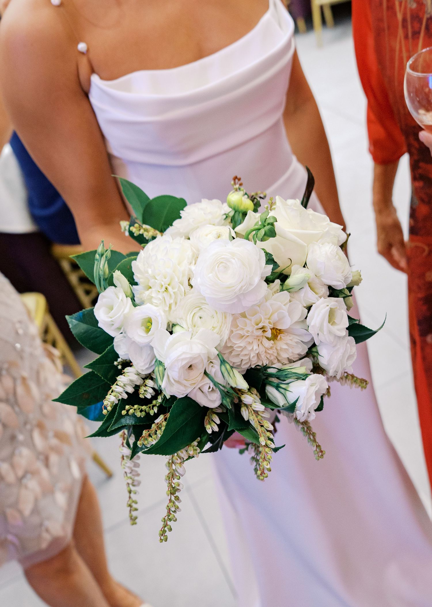 Close-up of an elegant white wedding bouquet with roses and greenery against a white dress.