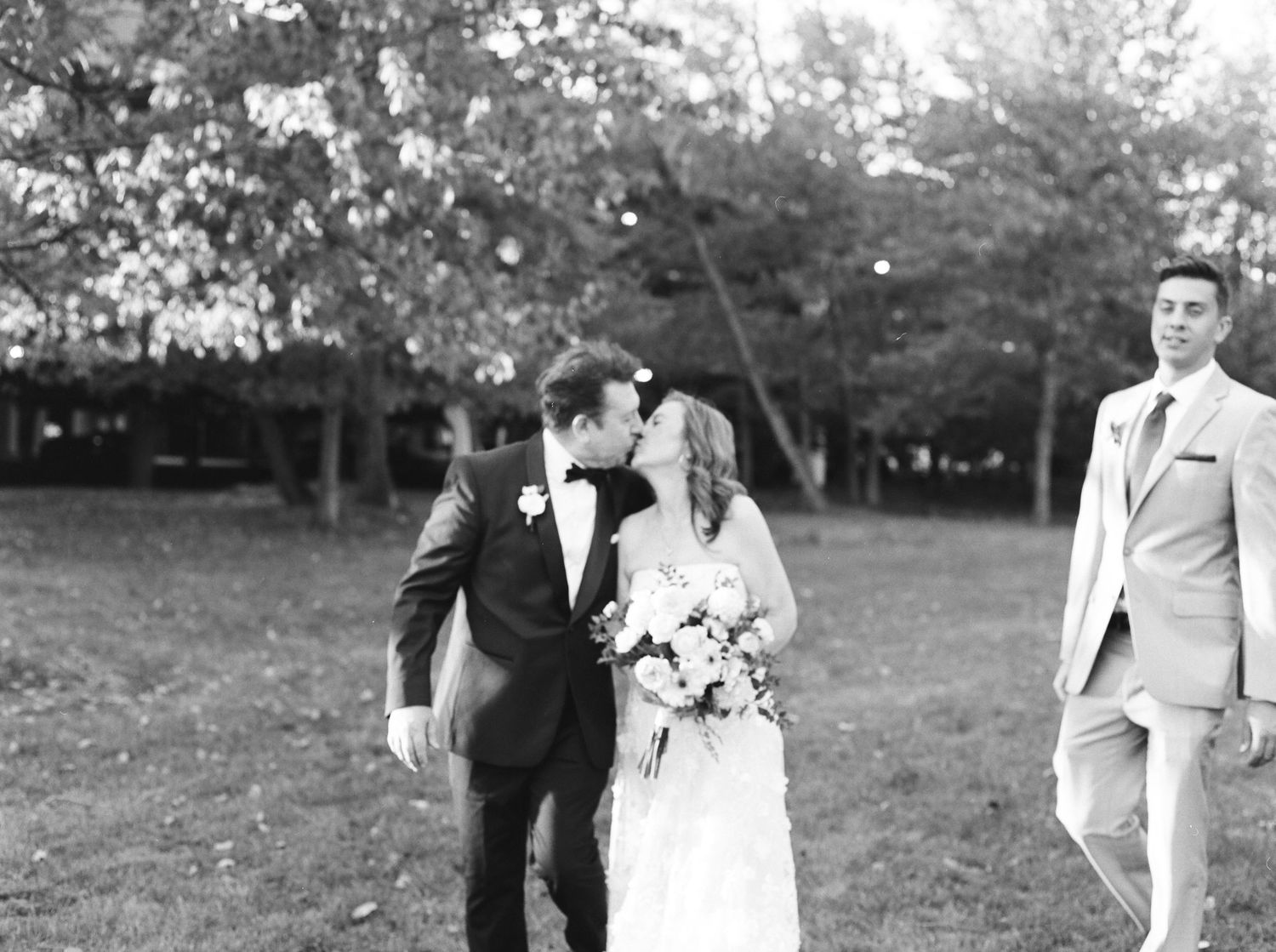 A wedding party walks through a grassy field on a sunny day.