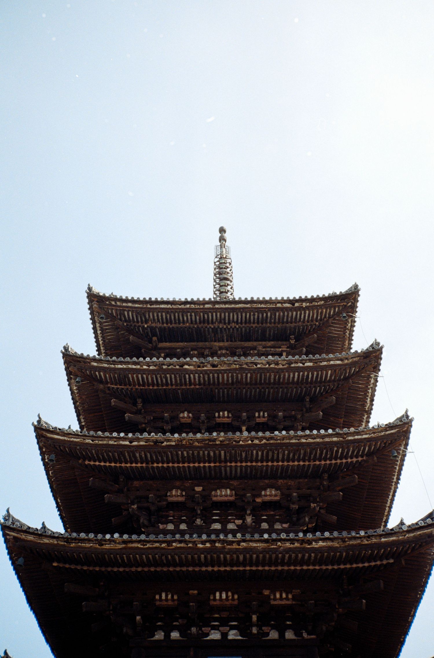 Traditional Japanese pagoda rooftops with multiple tiers silhouetted against a bright sky.