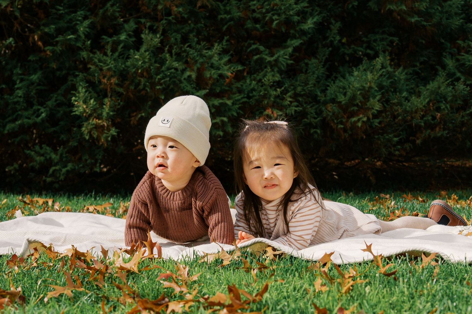 Two small children lying on a blanket outdoors enjoying a fall day together.
