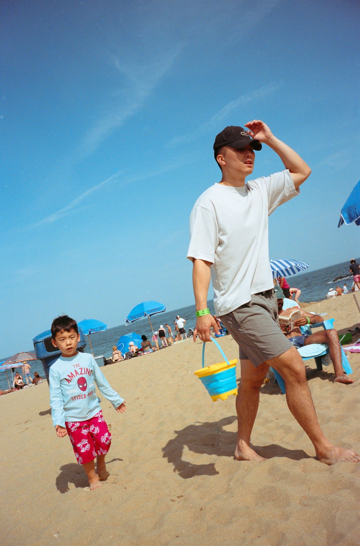 Beach scene with people playing and walking along sandy shoreline under bright blue sky.