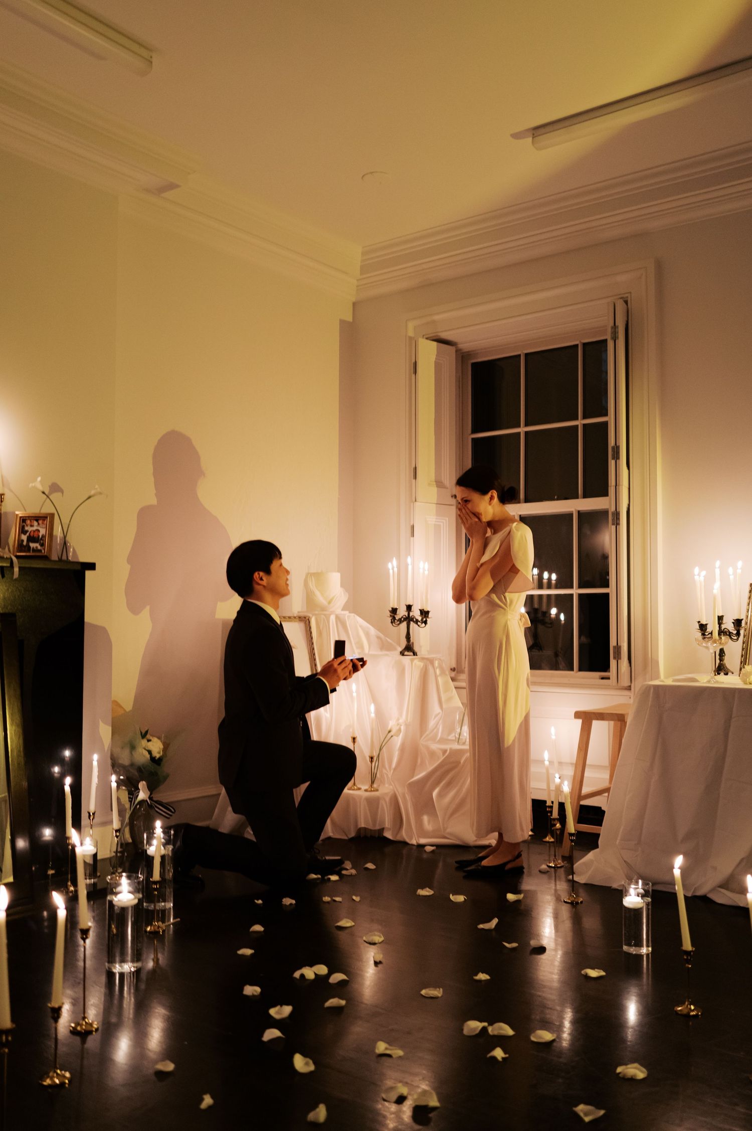 A candlelit proposal scene with rose petals scattered across a dark floor.
