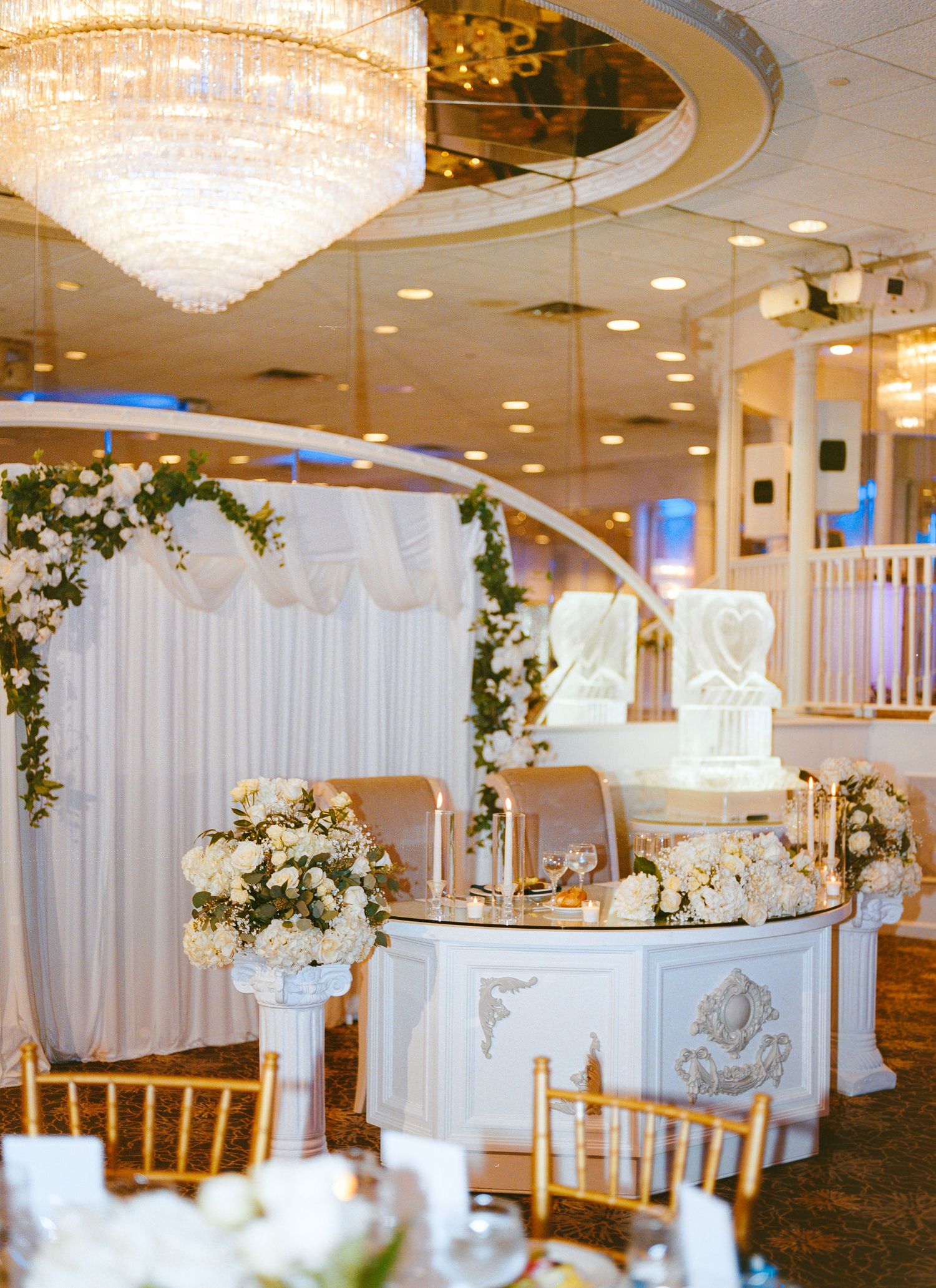 Luxurious wedding reception venue with crystal chandelier and white floral decorations.