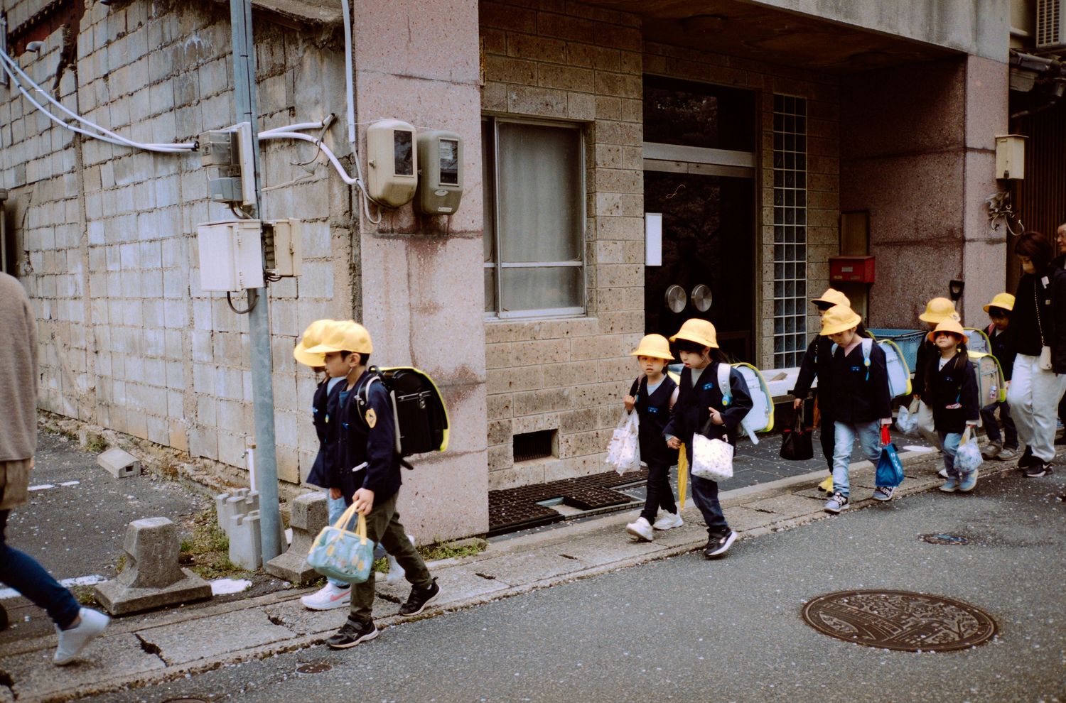 Students in yellow hats walking along a city street in Japan.