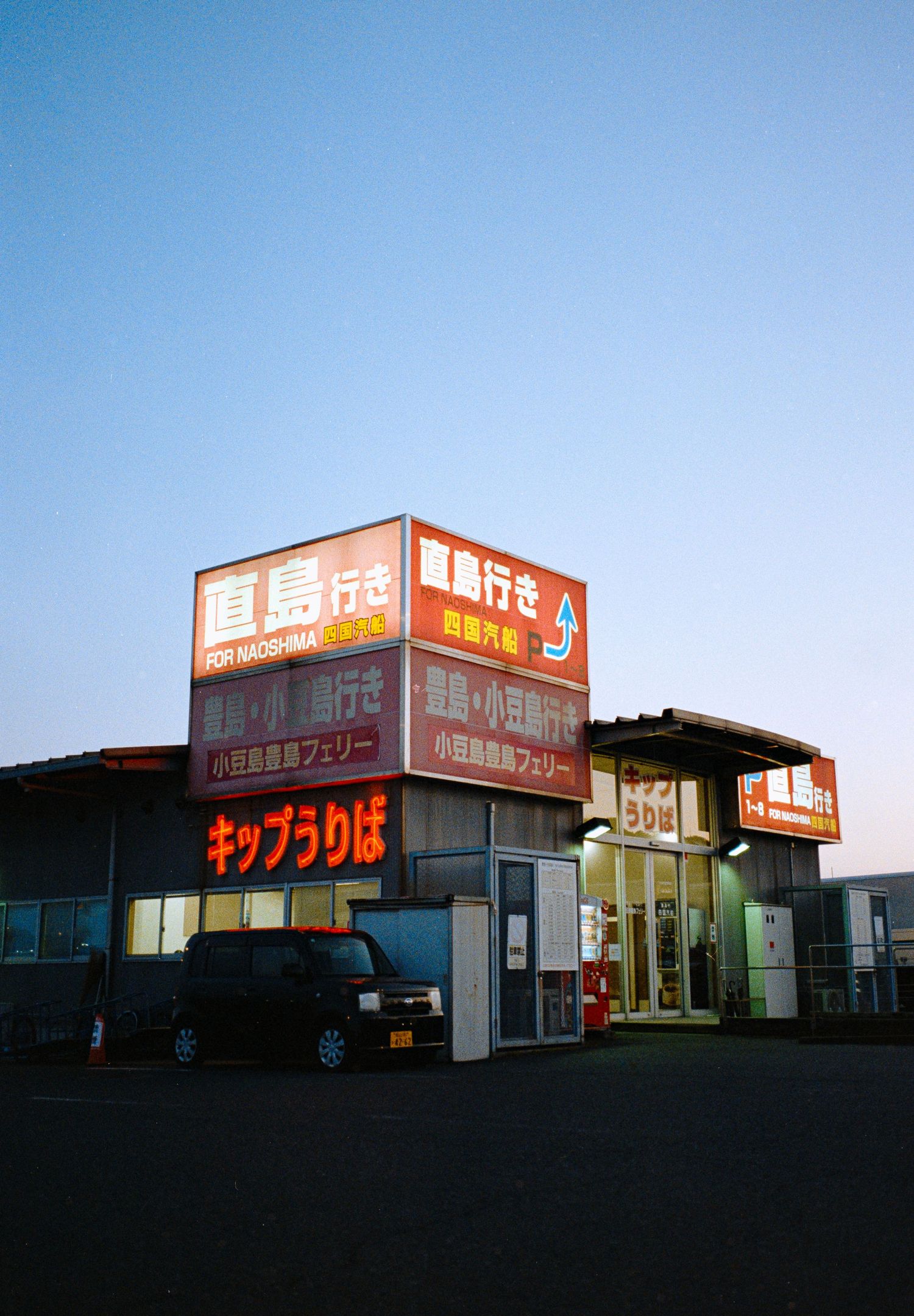 A row of illuminated Japanese retail storefronts at dusk with red signage.