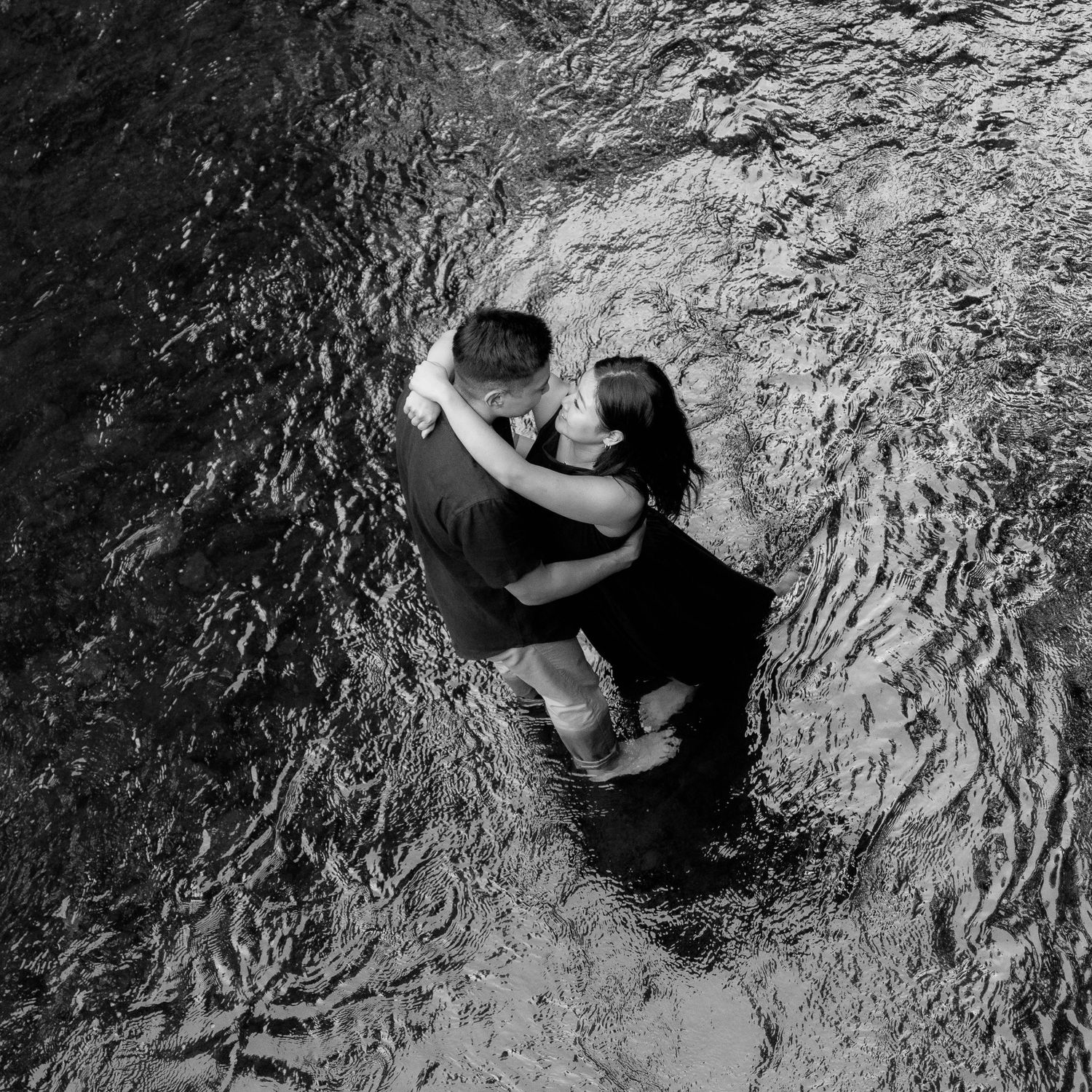 Aerial view of two people embracing while standing in rippling water.
