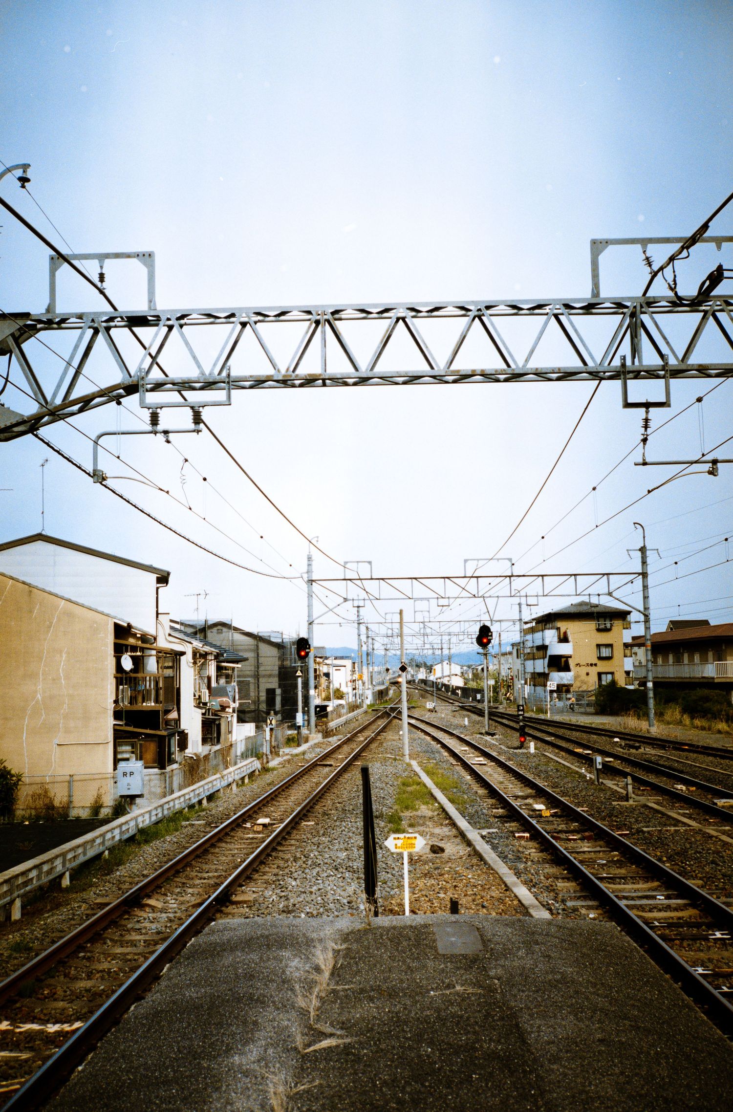 Train tracks with overhead power lines extend through a residential area in Japan.