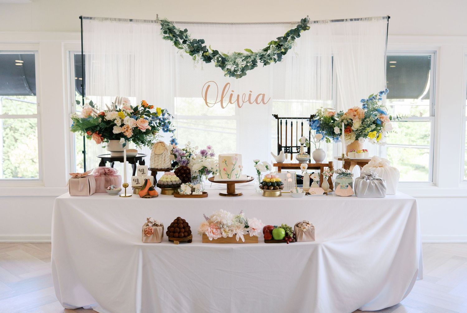 Elegant dessert table display with white linens, floral arrangements and cake stands at a wedding reception.