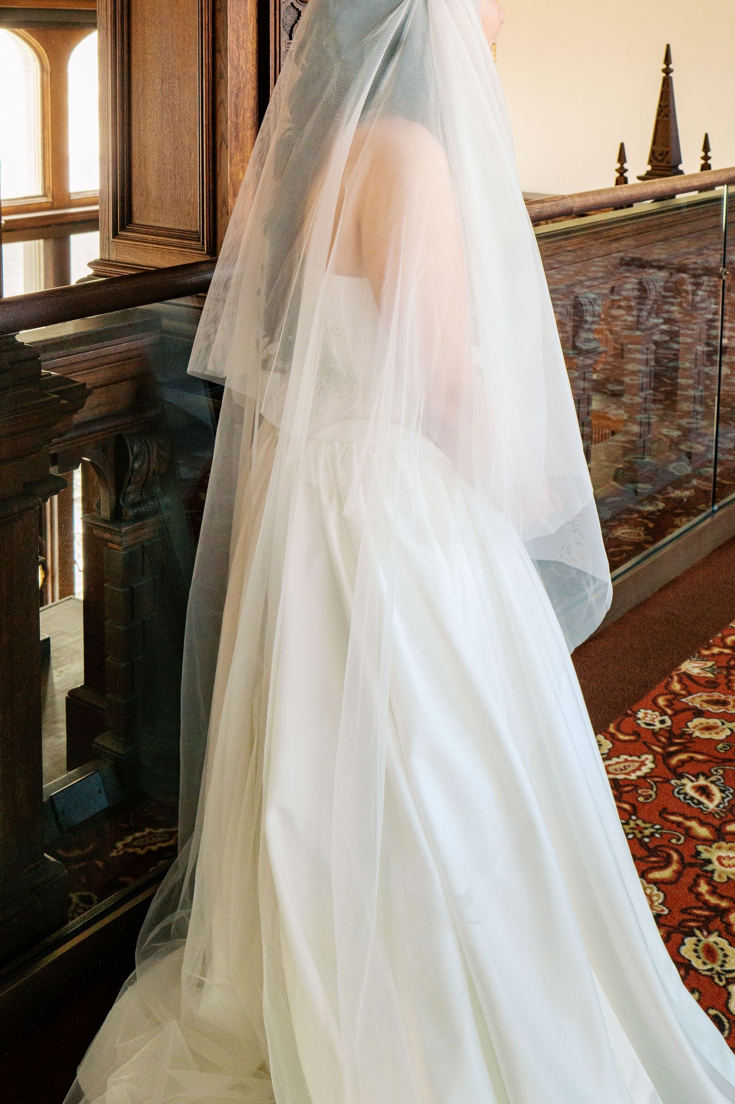 Flowing white wedding dress train with delicate tulle fabric cascades down elegant wooden staircase.